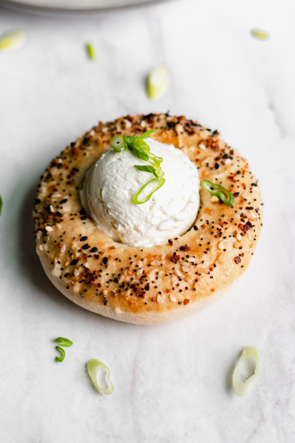 Close up shot of a bialy bagel with everything seasoning. Sliced green onions are on top.