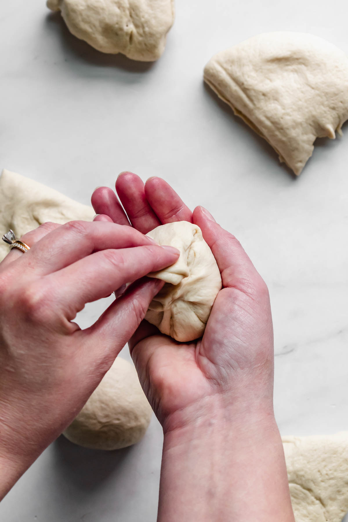 A hand pinches down the sides of the dough to create a ball.