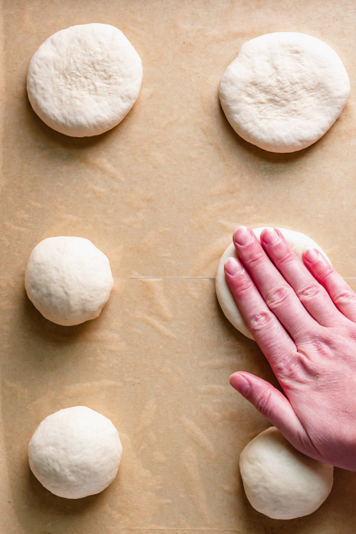A hand pushes down the dough into discs.