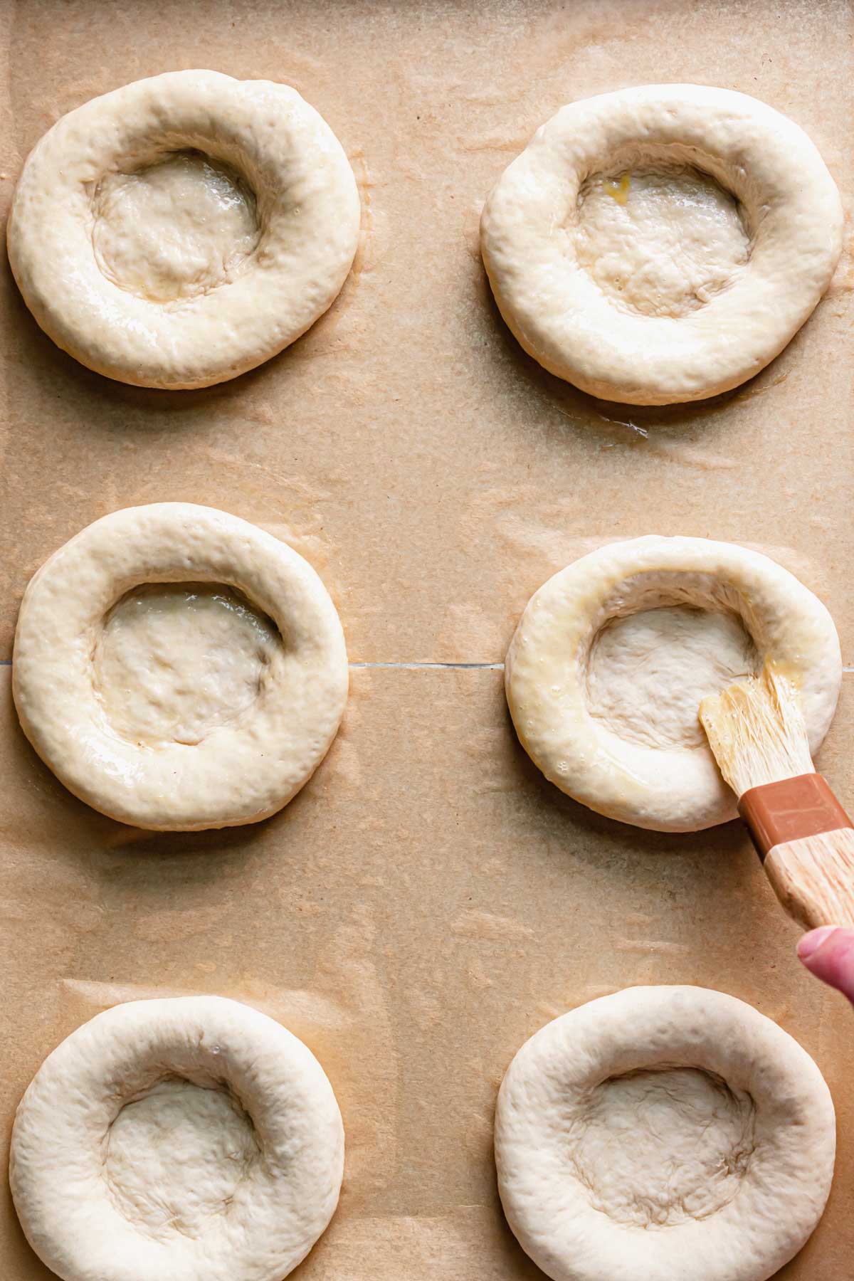 A pastry brush brushes egg wash onto the bialy bagel edges.
