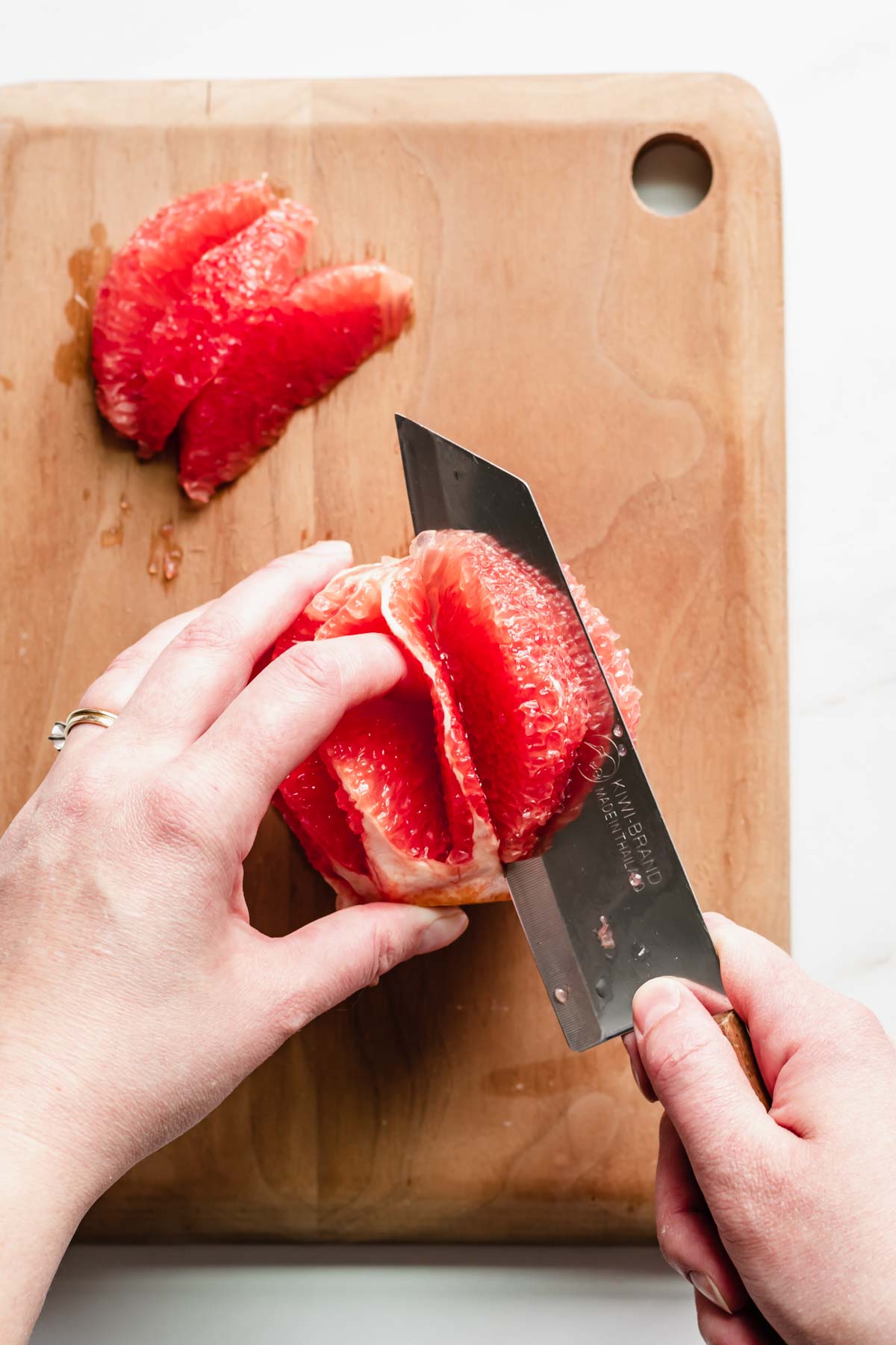 A knife cuts into a segment of grapefruit to create a garnish.