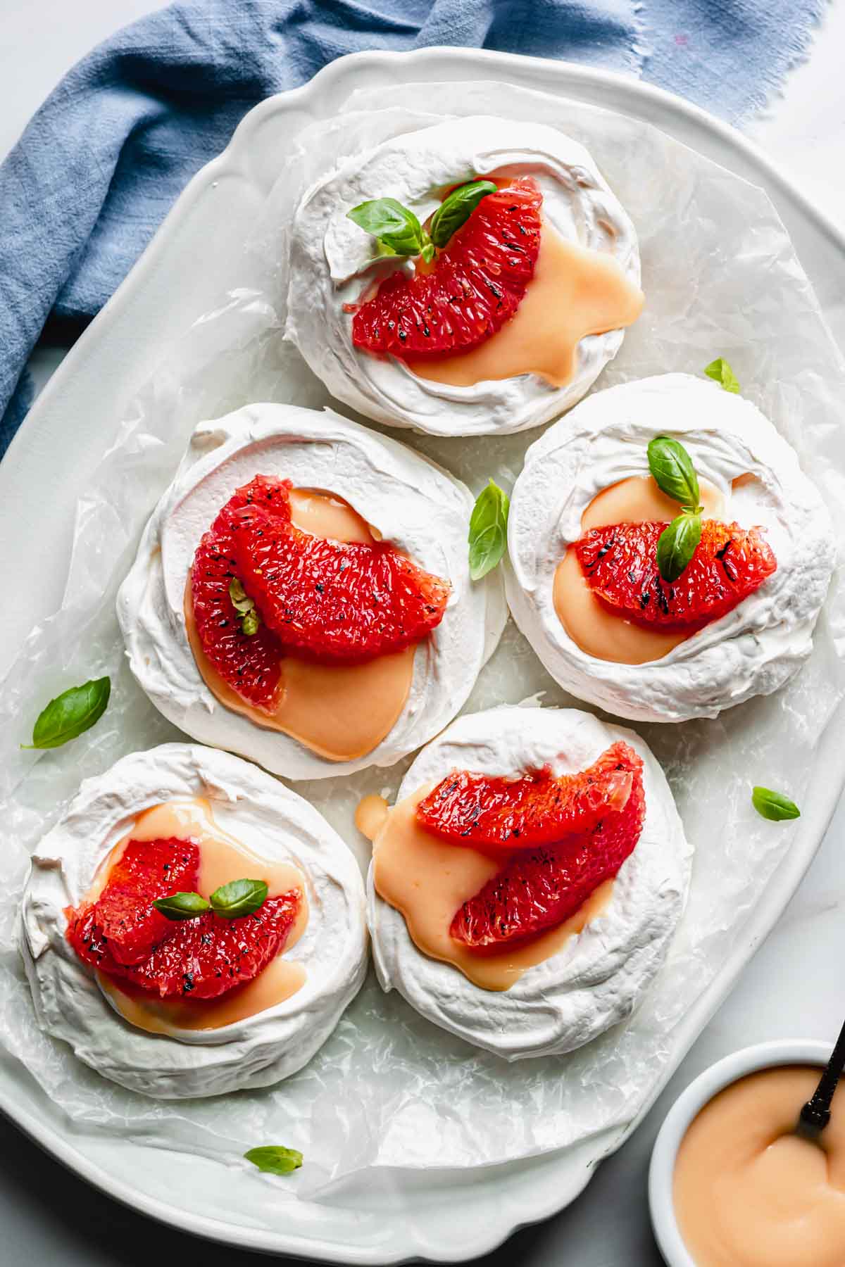 A platter with five assembled mini pavlova nests. Small pieces of basil garnish the platter.