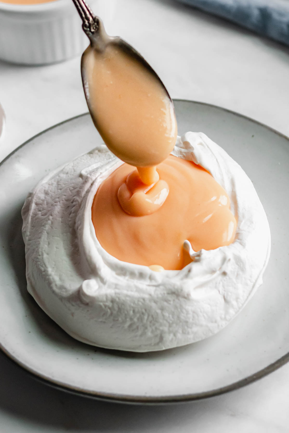 A spoon pours grapefruit curd into a pavlova nest.