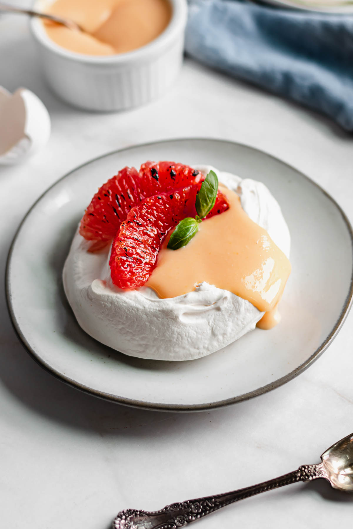 Individual pavlova filled with grapefruit curd and two slices of grapefruit. The curd drips over one side.