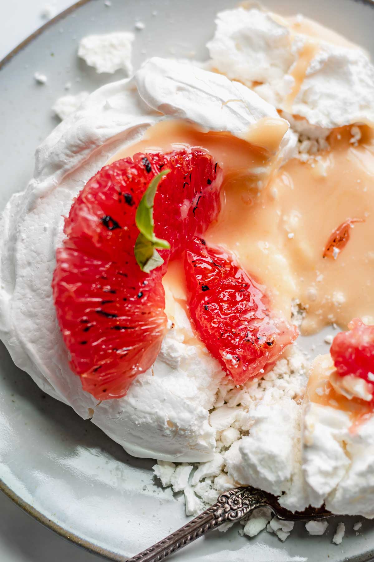 Close up of a mini pavlova broken into with two segments of grapefruit on top. The curd falls out of the side.