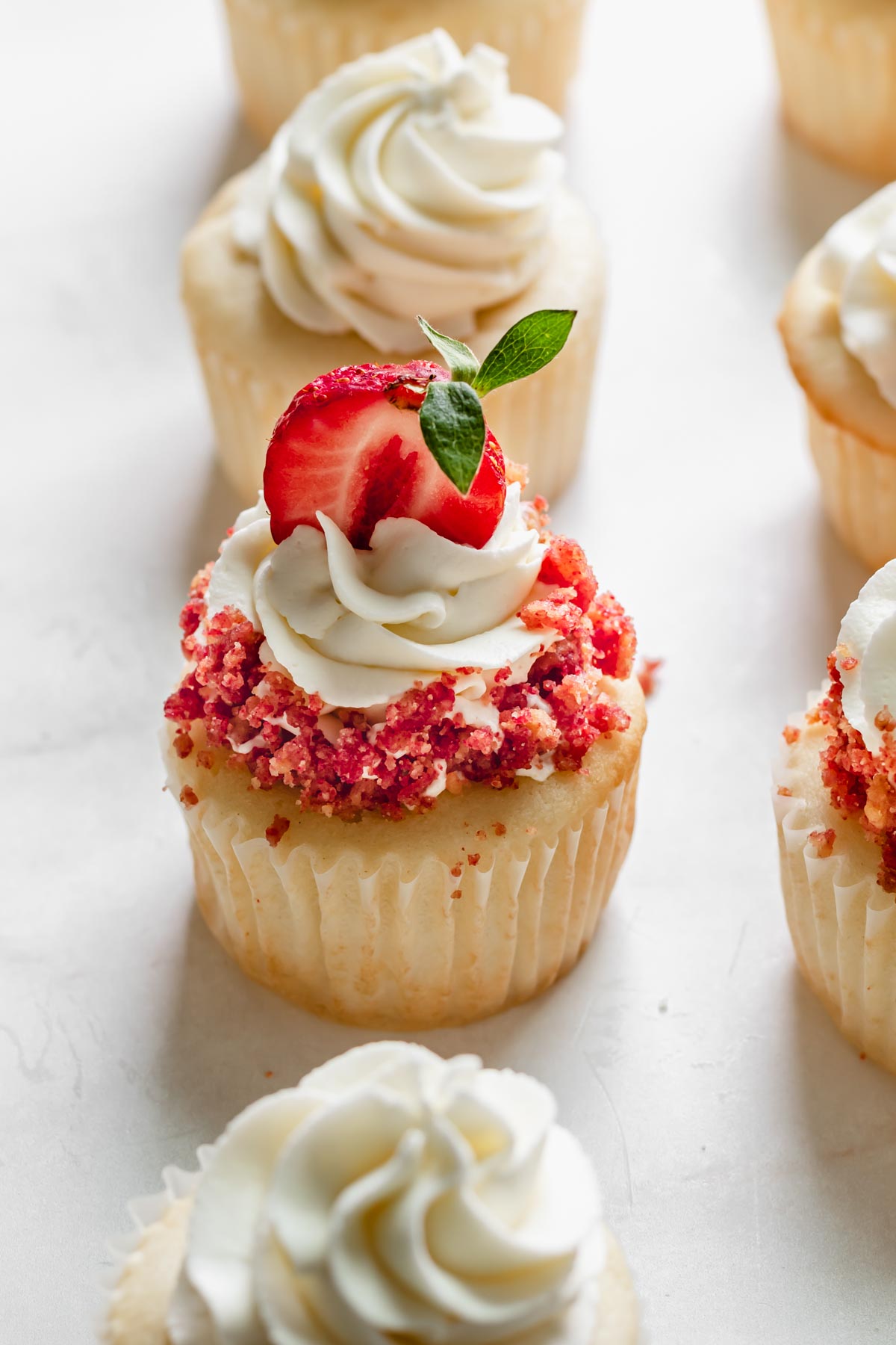 One finished strawberry crunch cupcakes surrounded by other frosted cupcakes.
