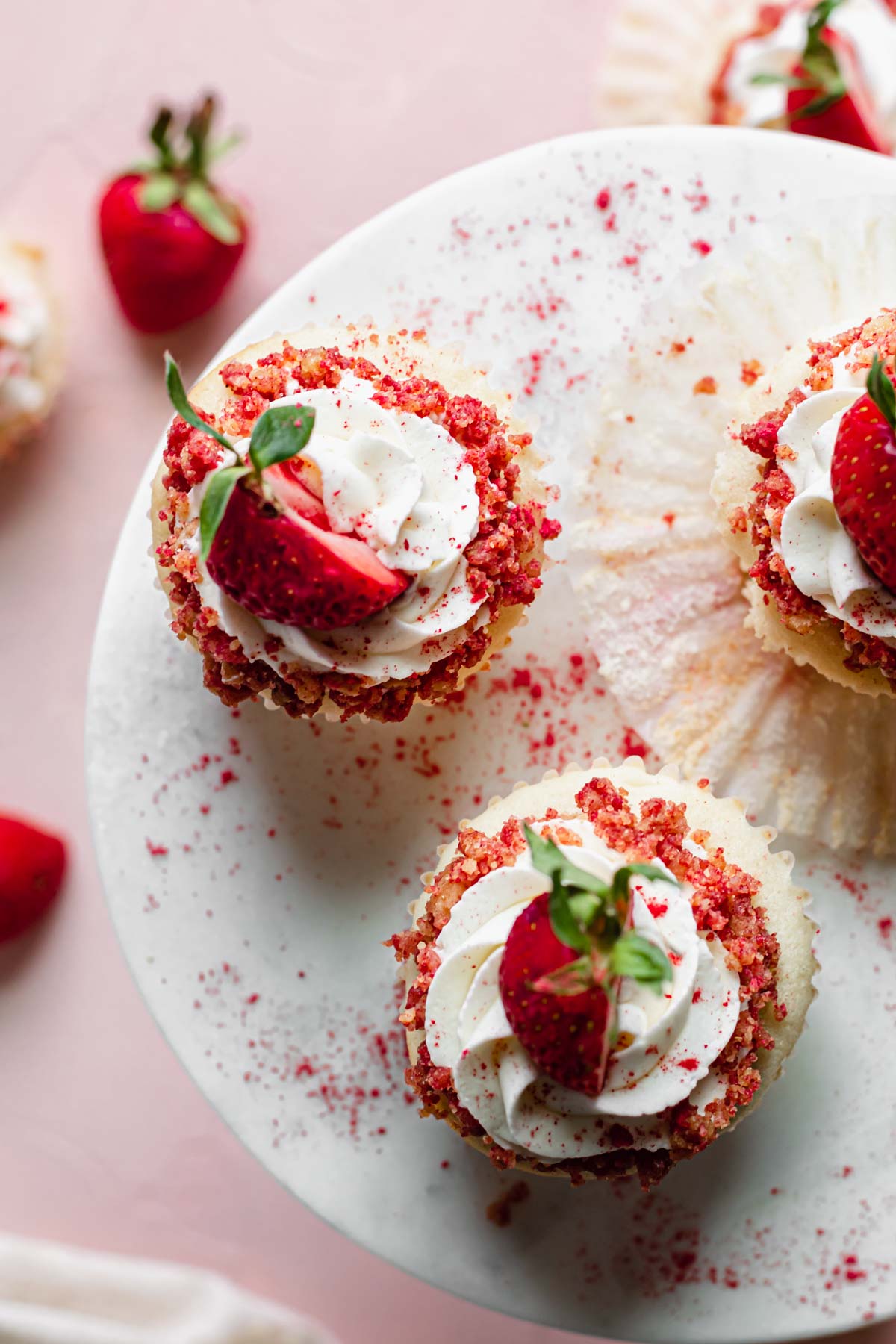 Overhead shot of three strawberry crunch cupcakes on a cake stand.