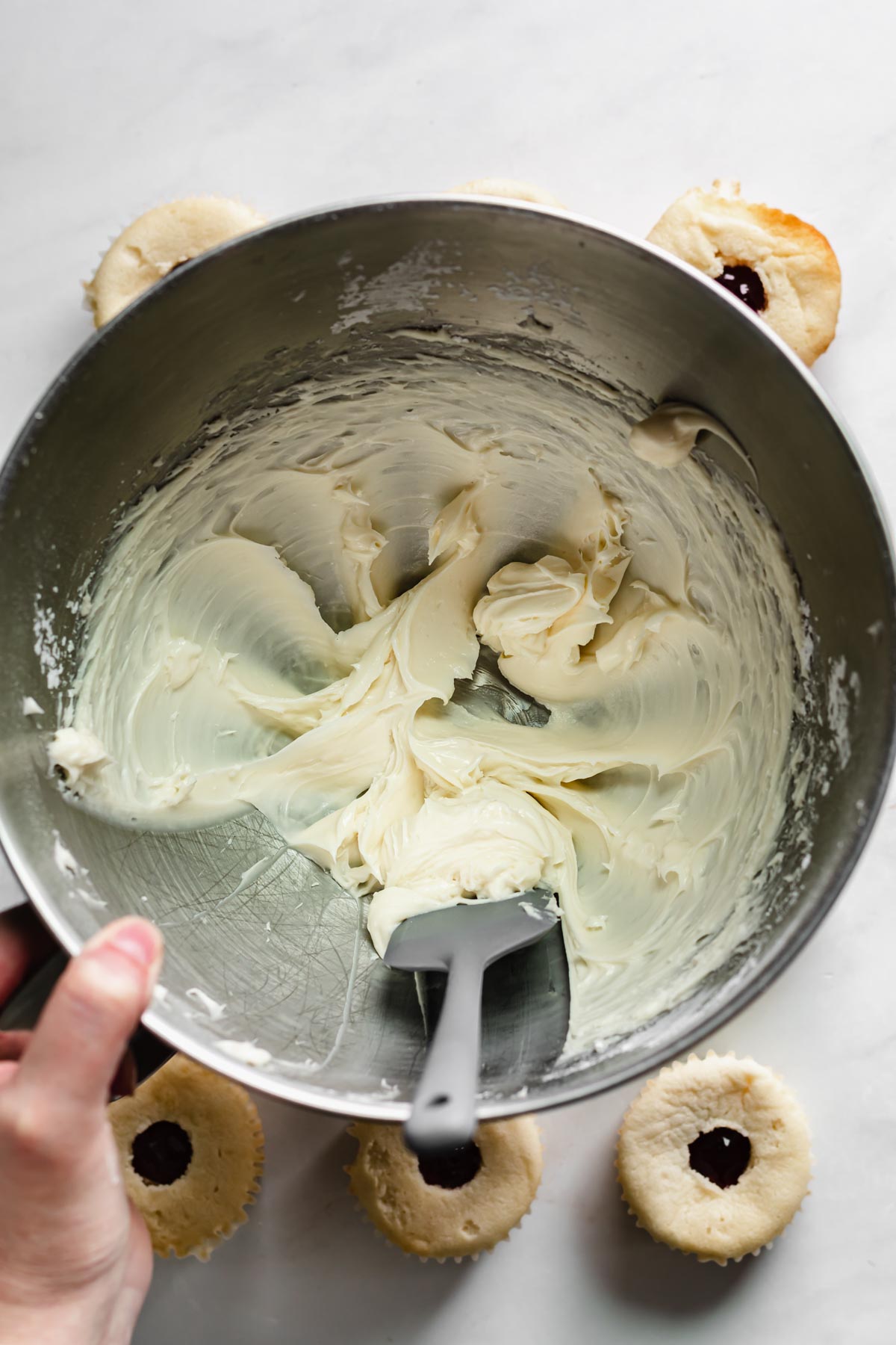 Creamed cream cheese being scraped off the sides of a mixing bowl.