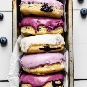 Glazed blueberry donuts lined up in a pan.