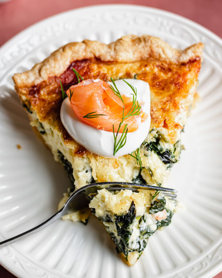 A slice of smoked salmon and spinach quiche on a plate with a fork in it.
