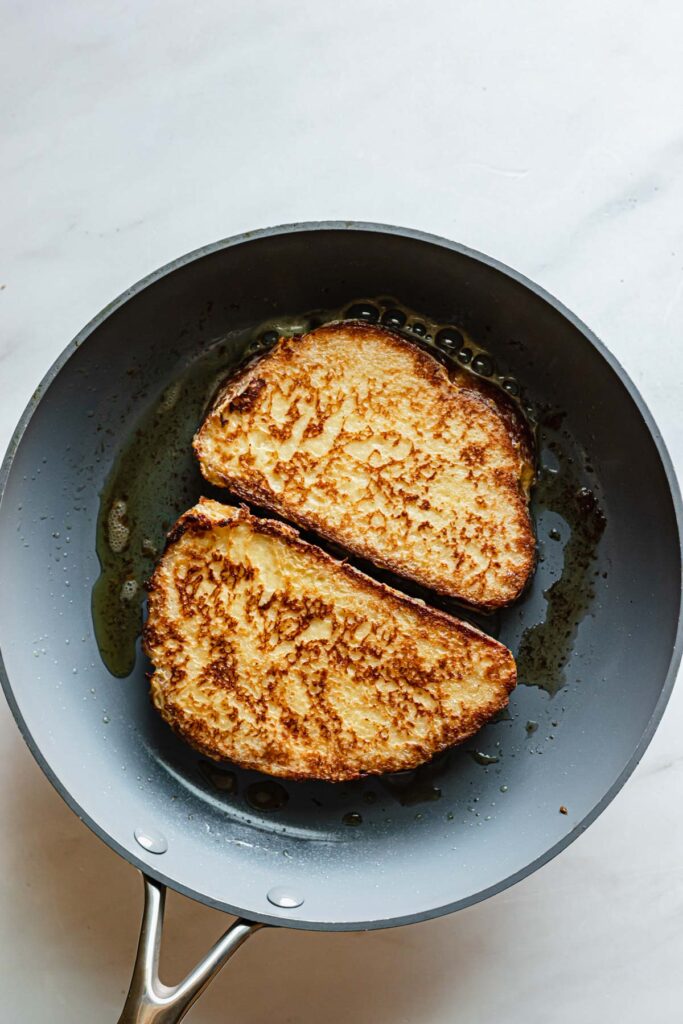 Two pieces of caramelized French toast in a pan.