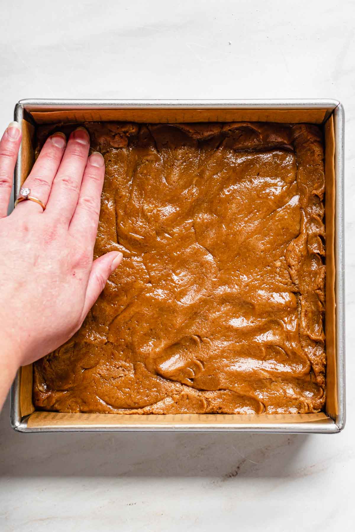 A hand presses the batter into the pan.