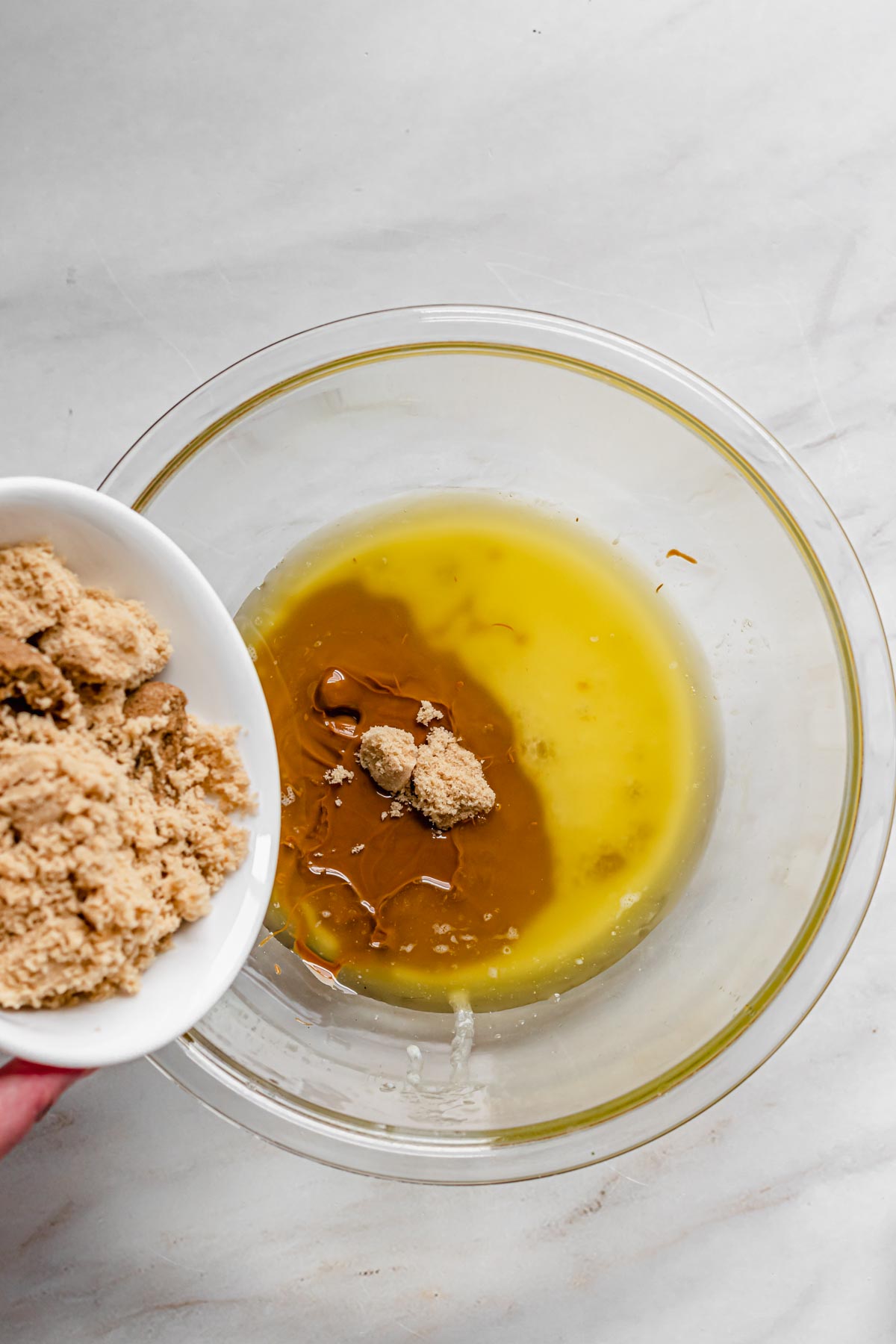 Brown sugar pours into a bowl of melted butter and cookie butter.