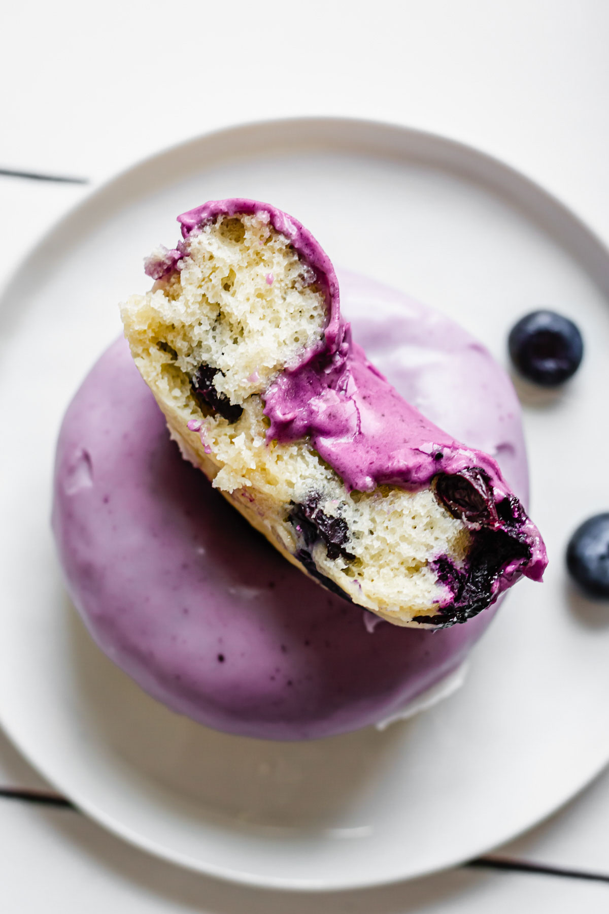 Two glazed blueberry donuts on a plate with the top one exposing the center of the donut.