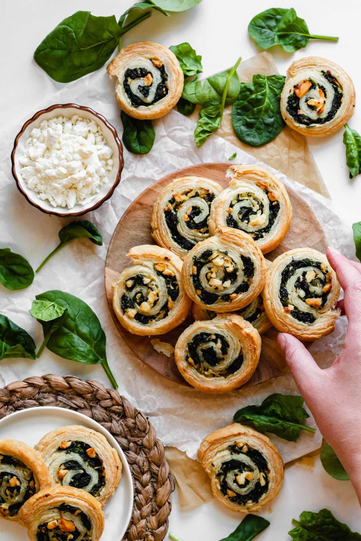 Spinach feta pinwheels layered on a plate. A hand reaches in.