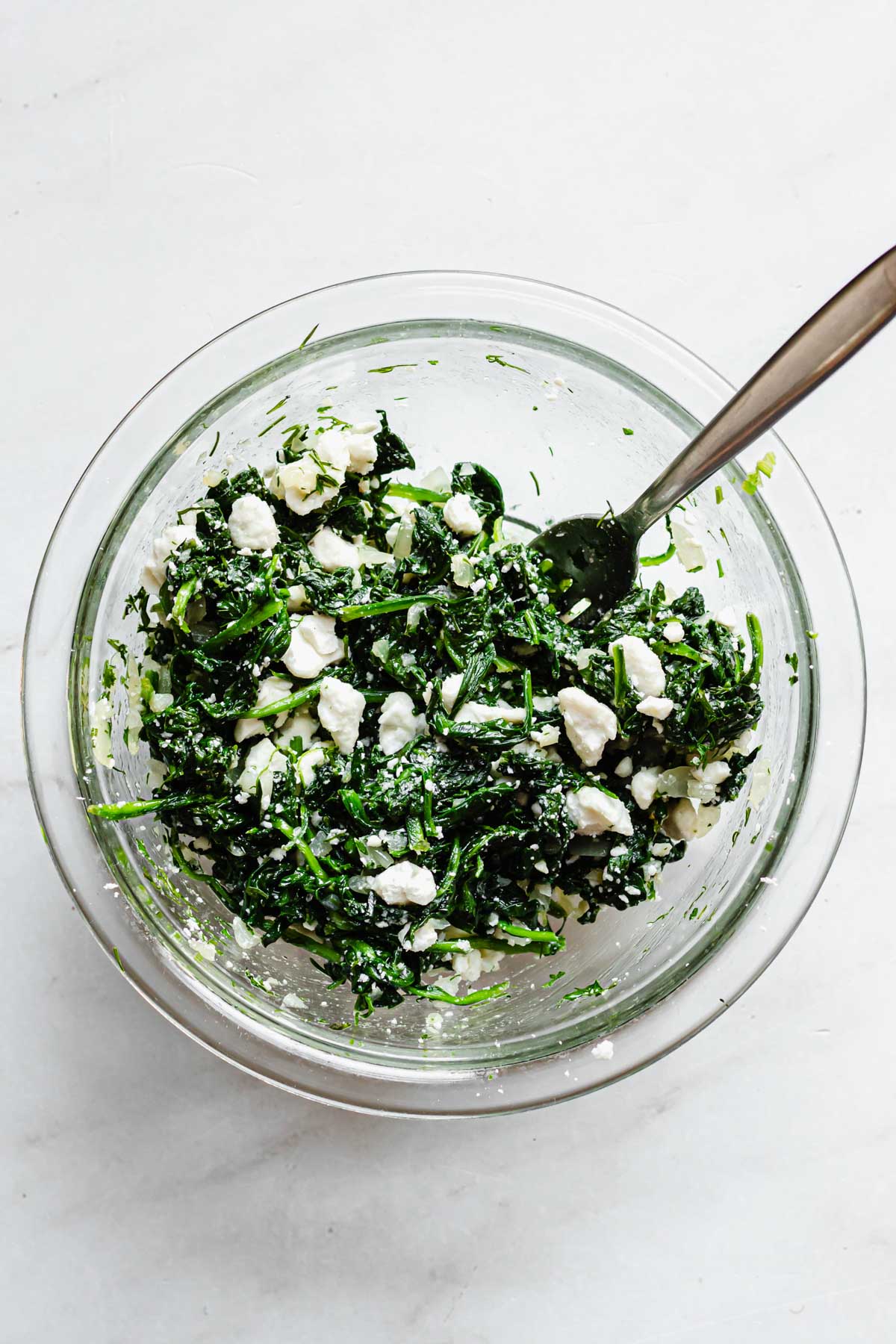 Feta cheese being mixed into the spinach.
