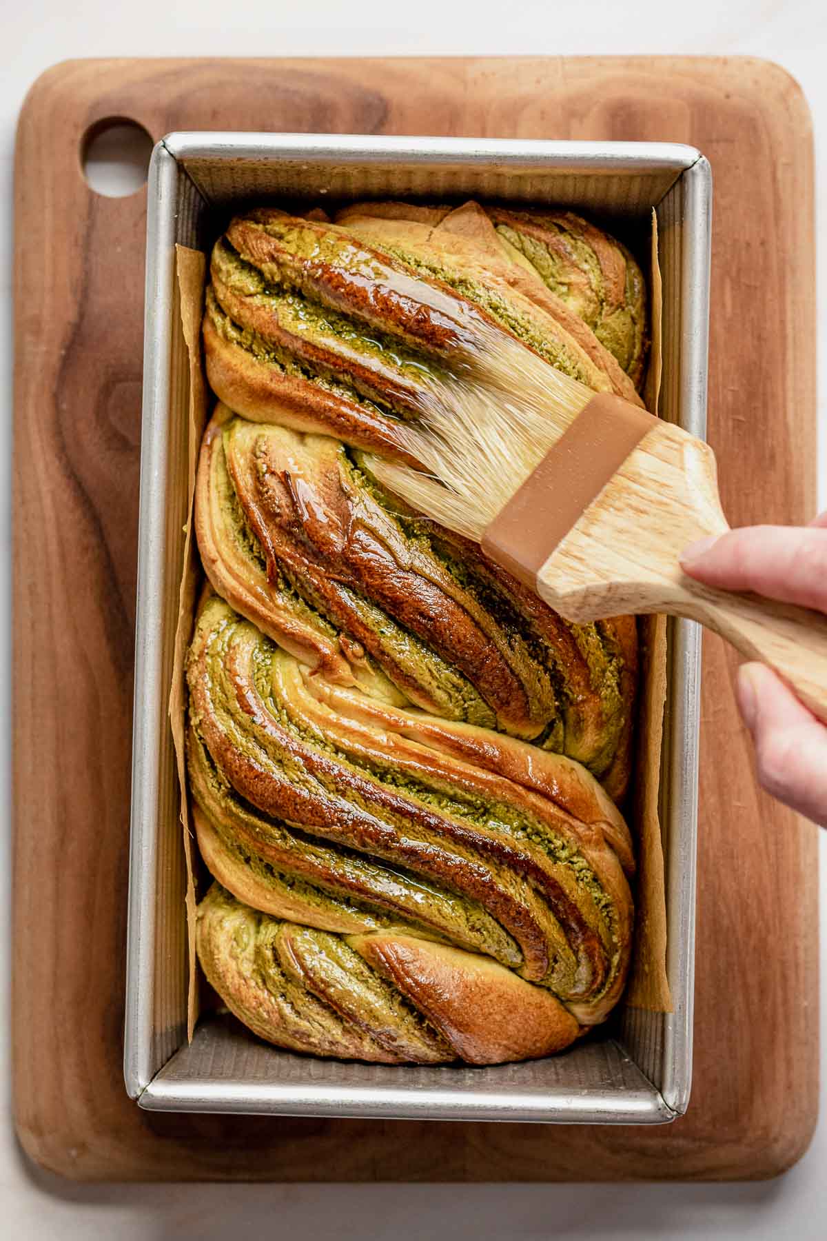 A hand brushes on simple syrup on the baked babka.
