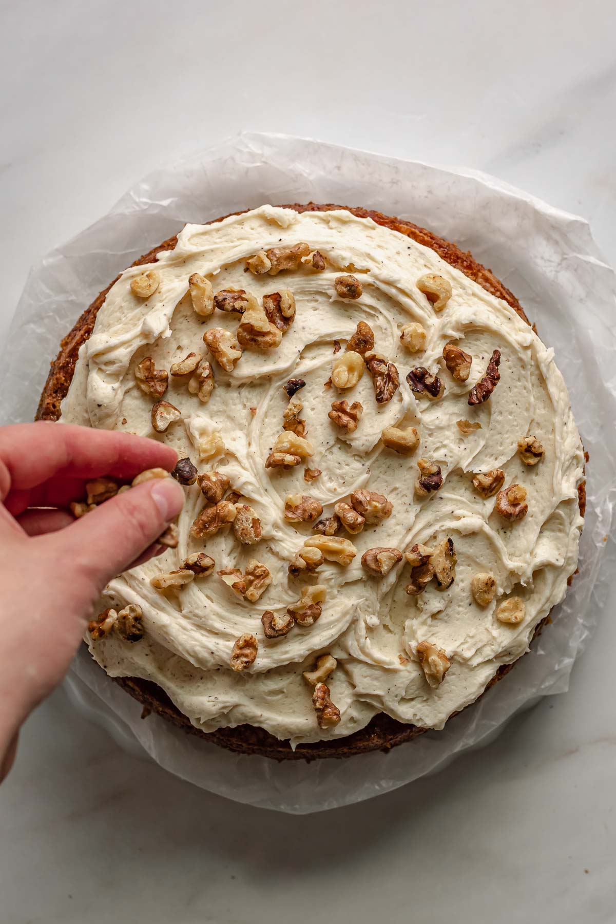 A hand sprinkles on chopped pecans to the frosting.