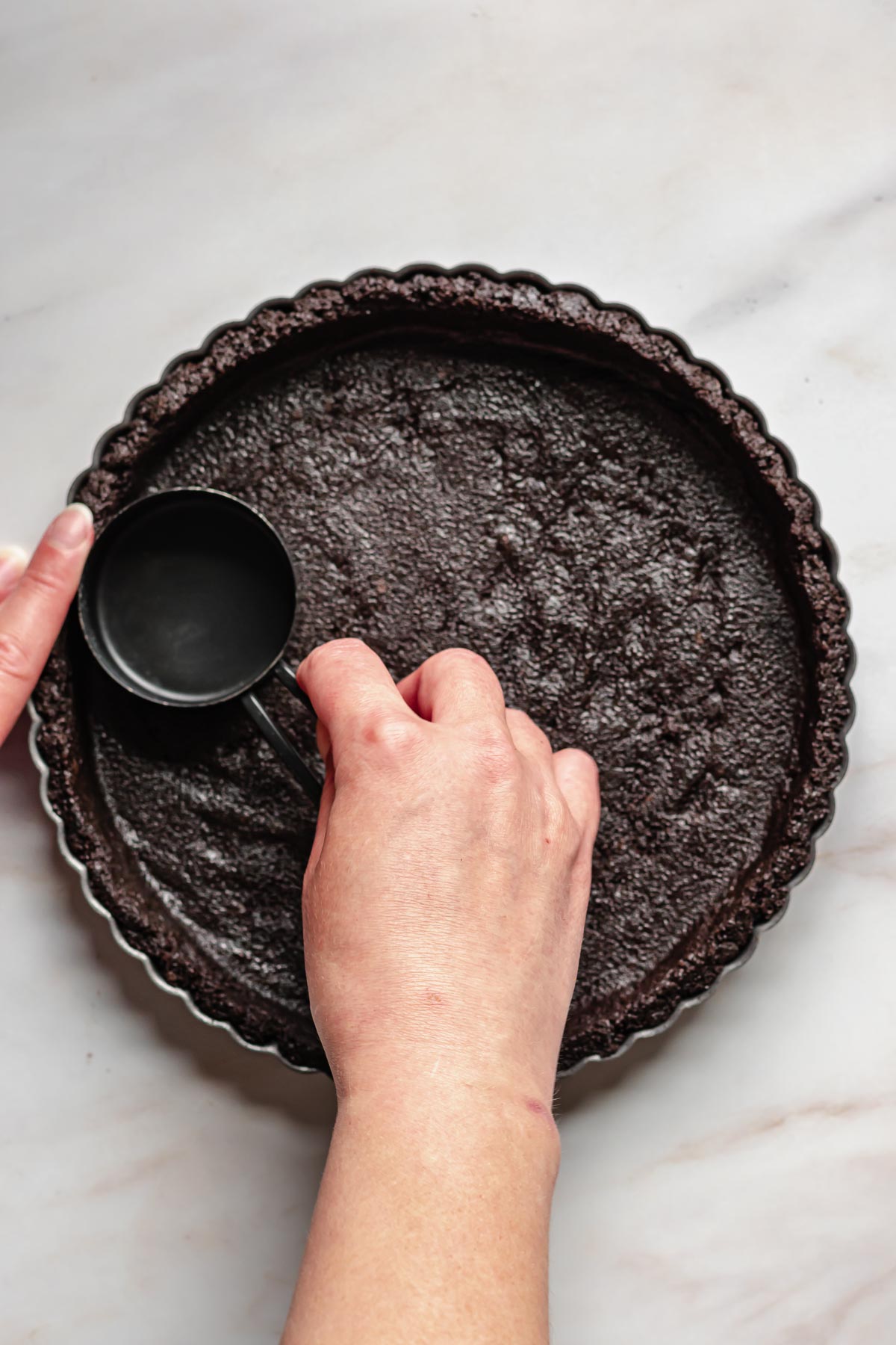 A hand forms the graham cracker crust in the tart pan.
