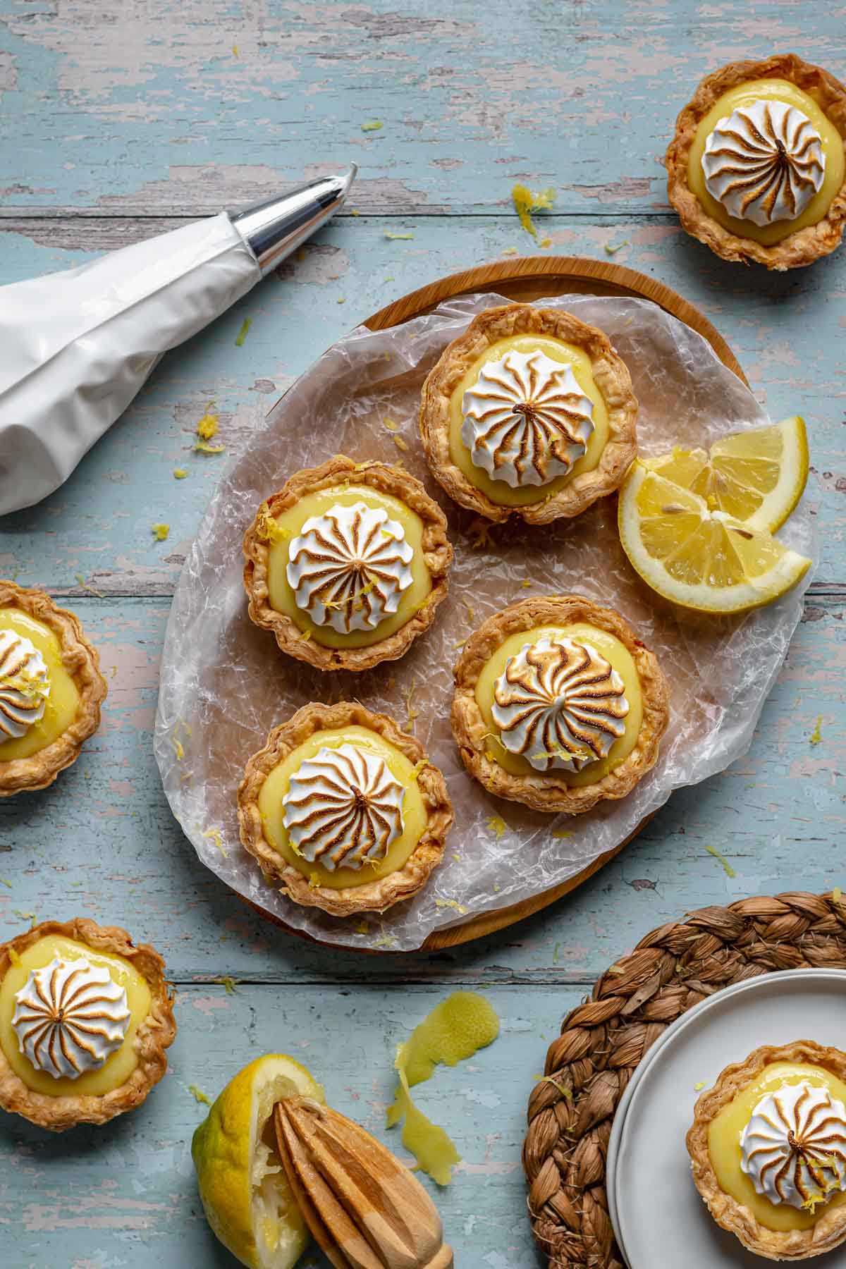 Mini lemon meringue tarts on a platter with lemons scattered around.