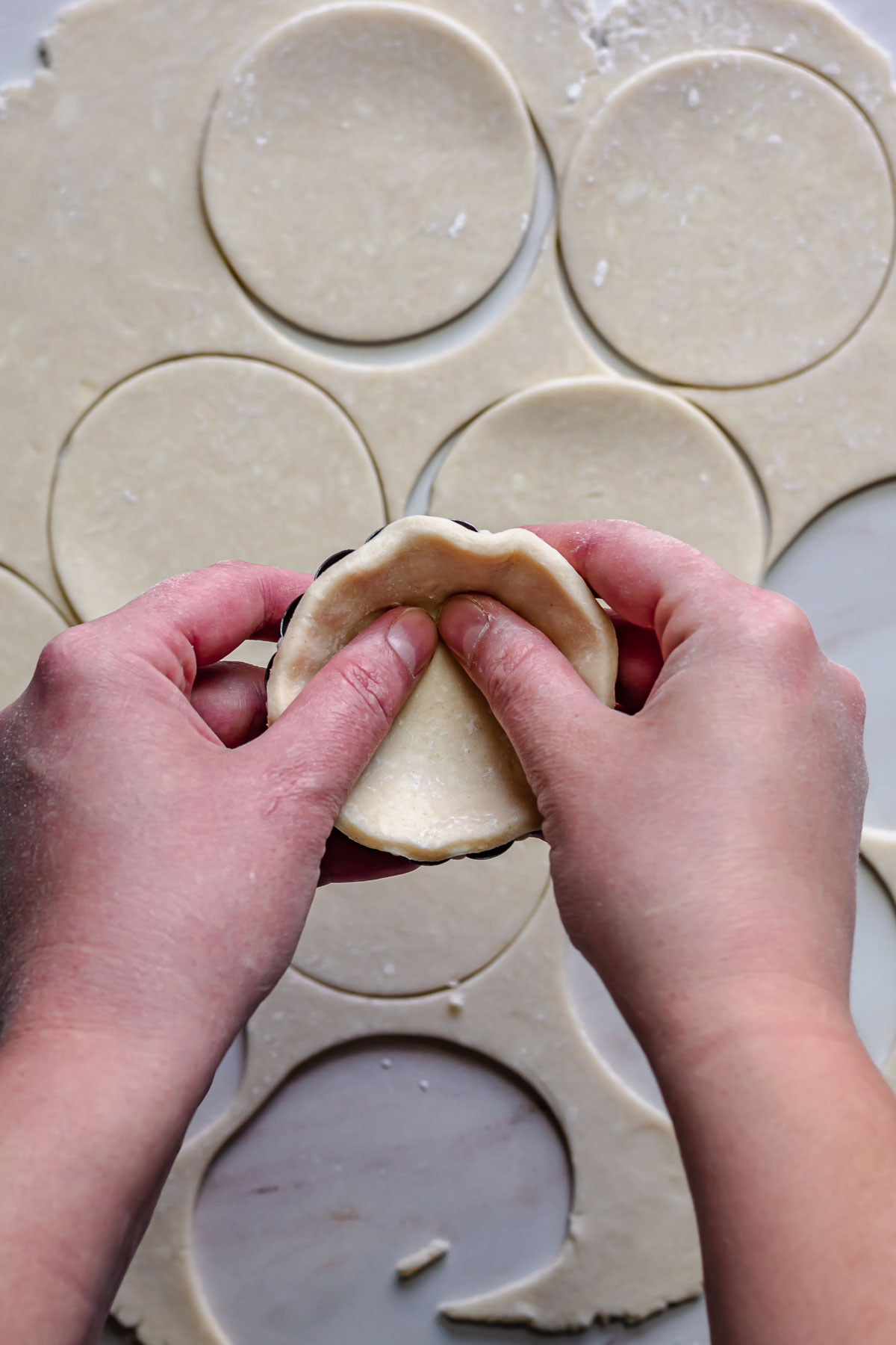 Hands adding dough to a tartlet pan.