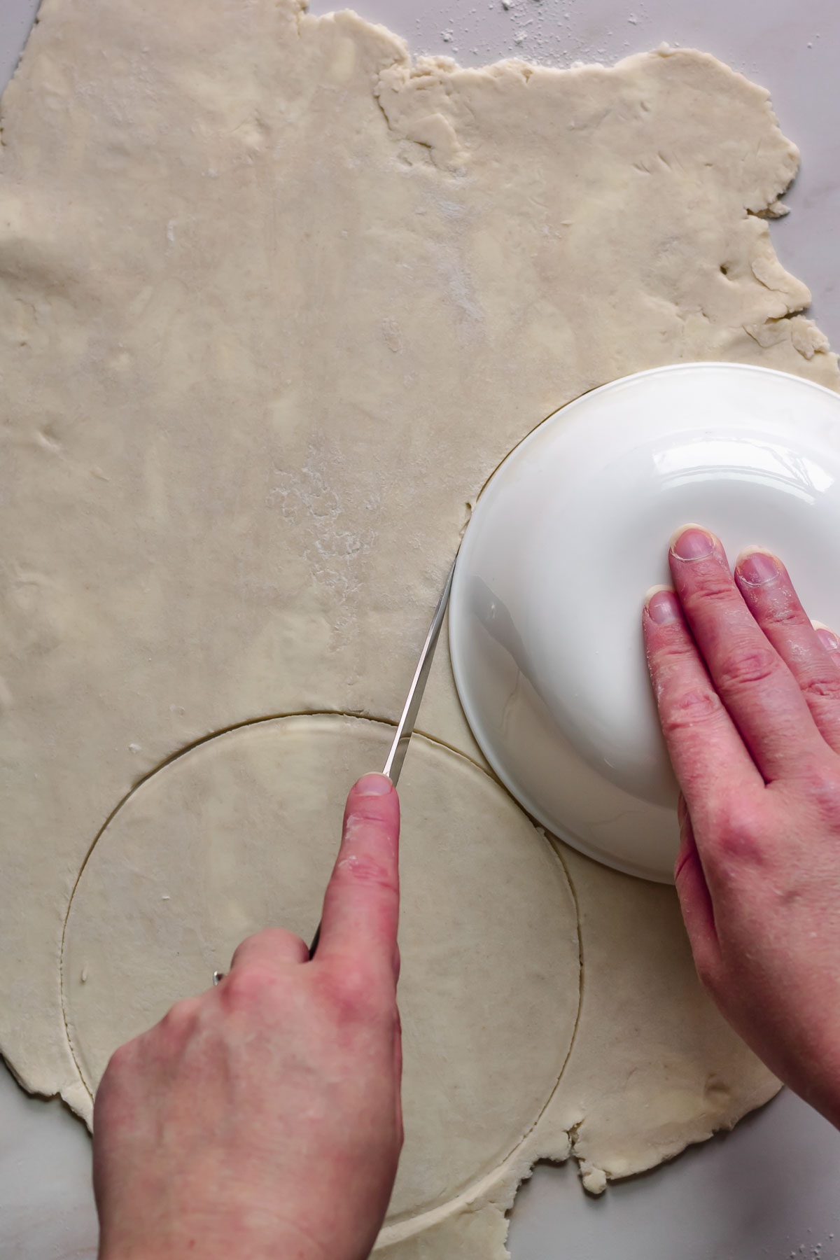 Cutting out pie crust with a bowl and knife.