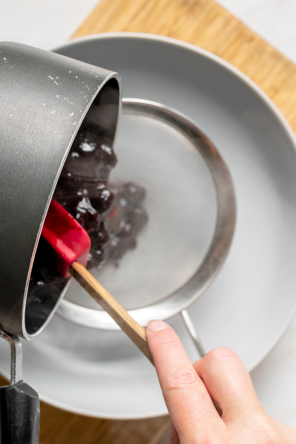 Cooked blueberries being poured through a sieve.