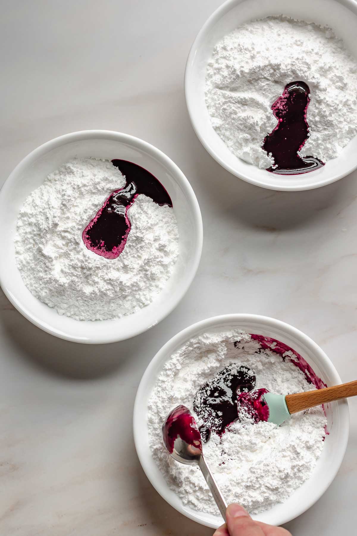 Bowls of powdered sugar with blueberry puree in them.