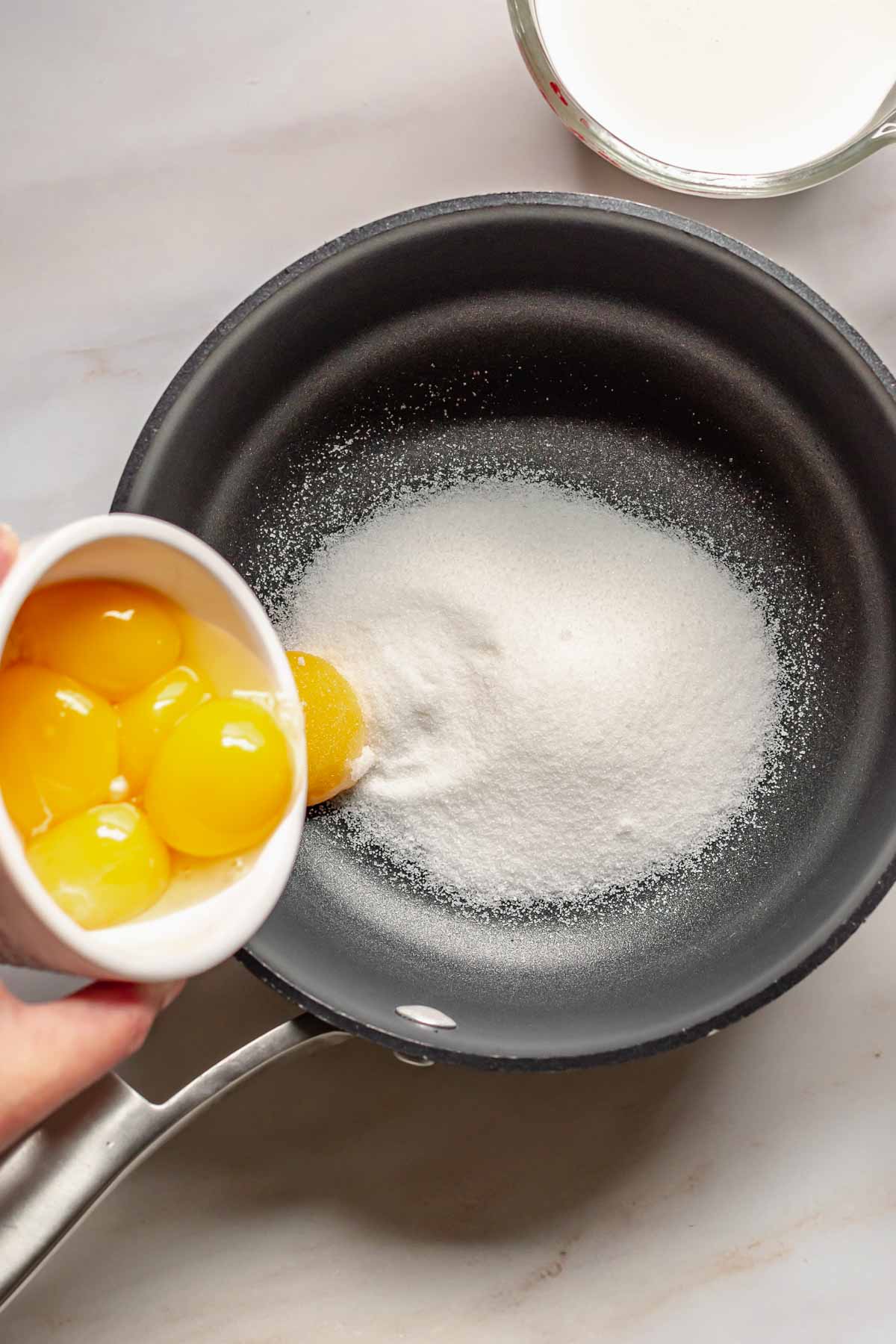 Egg yolks adding to sugar in a pot.