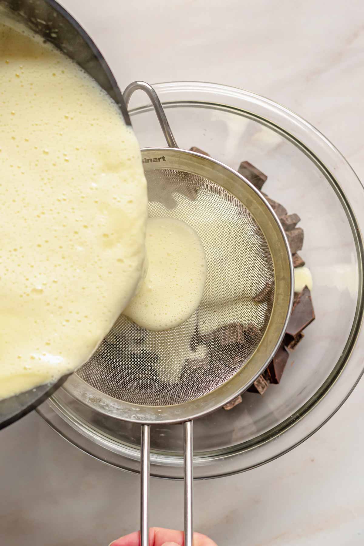 Custard cream pouring through a sieve into a bowl of chocolate.