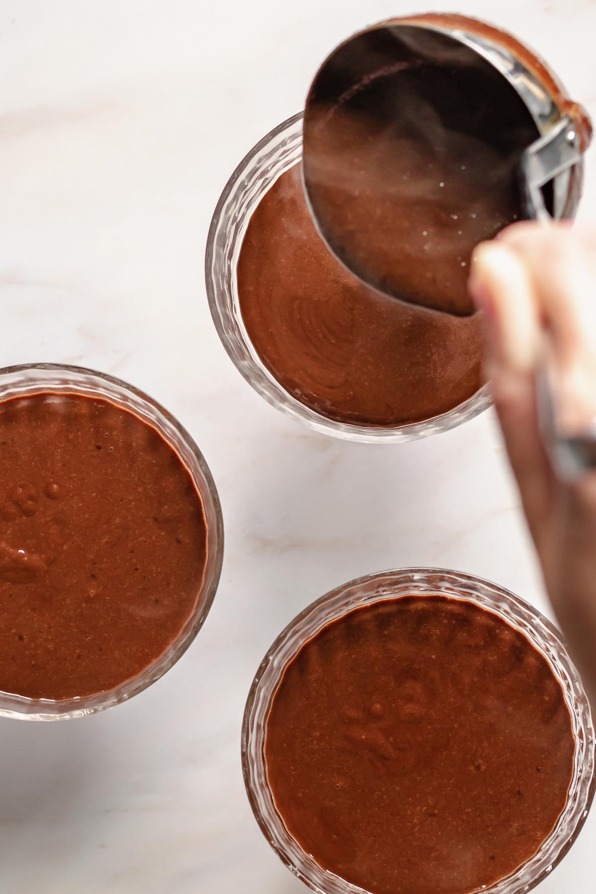 A ladle pours chocolate mixture into coupe glasses.