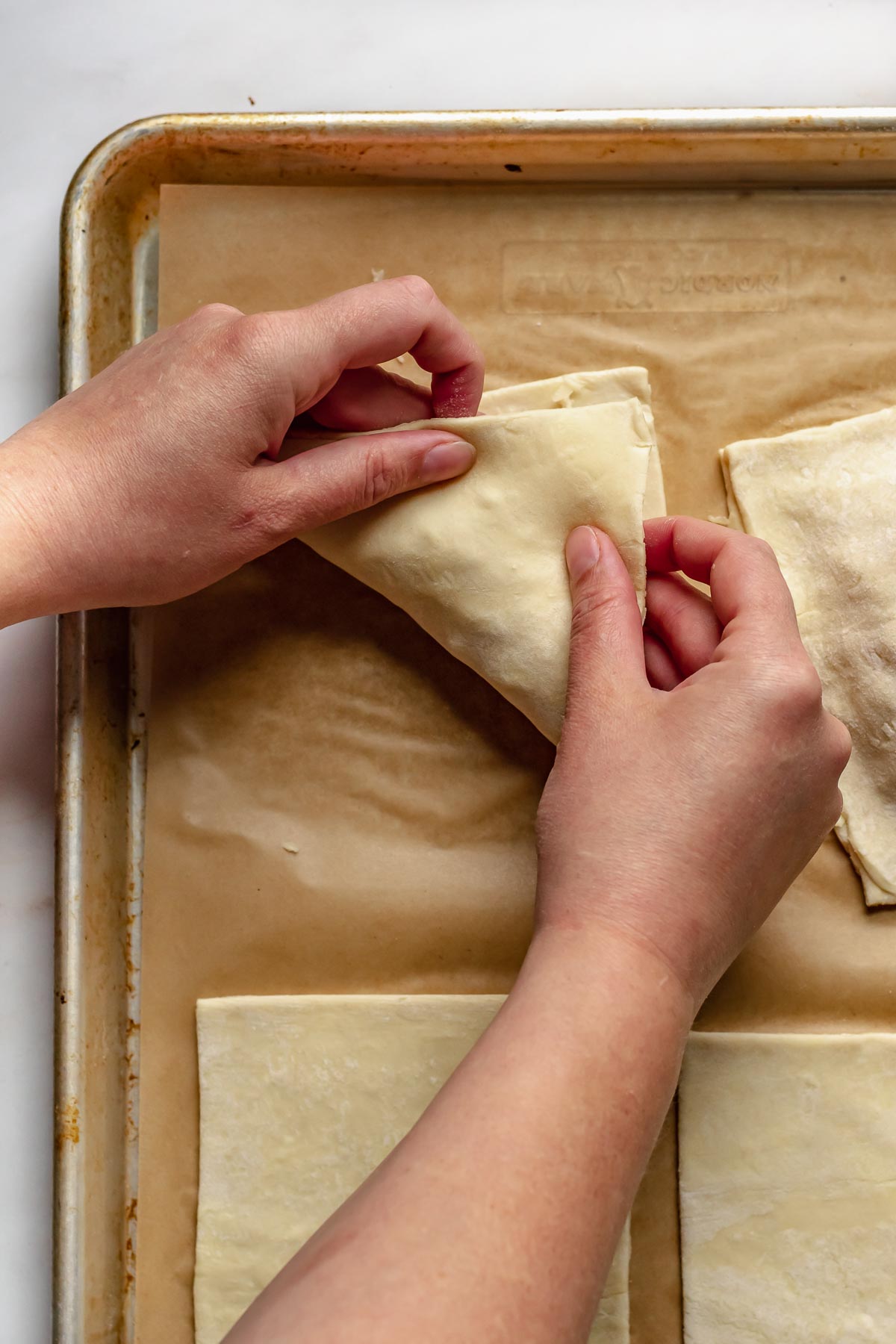 Hands close the pastry over the ham and cheese filling.