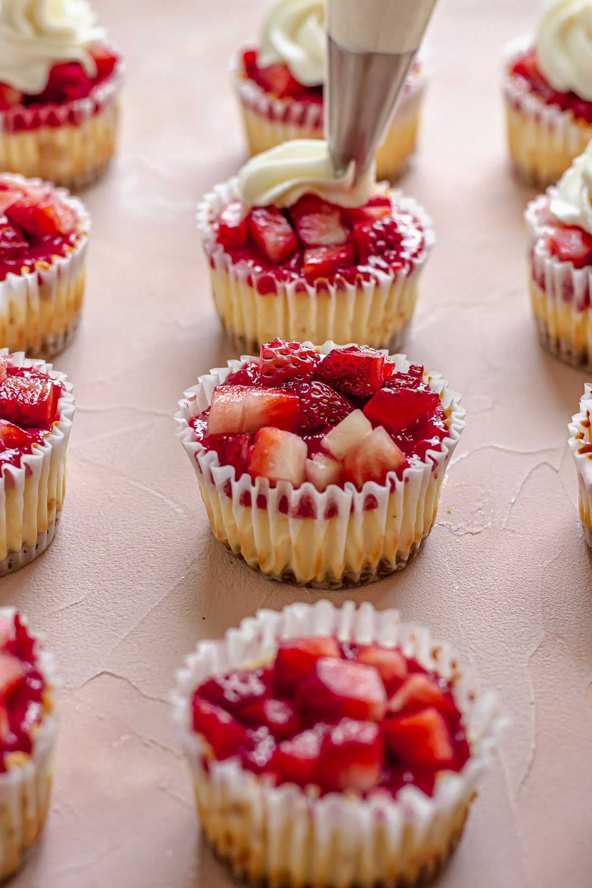 Whipped cream is piped onto the mini strawberry cheesecakes.