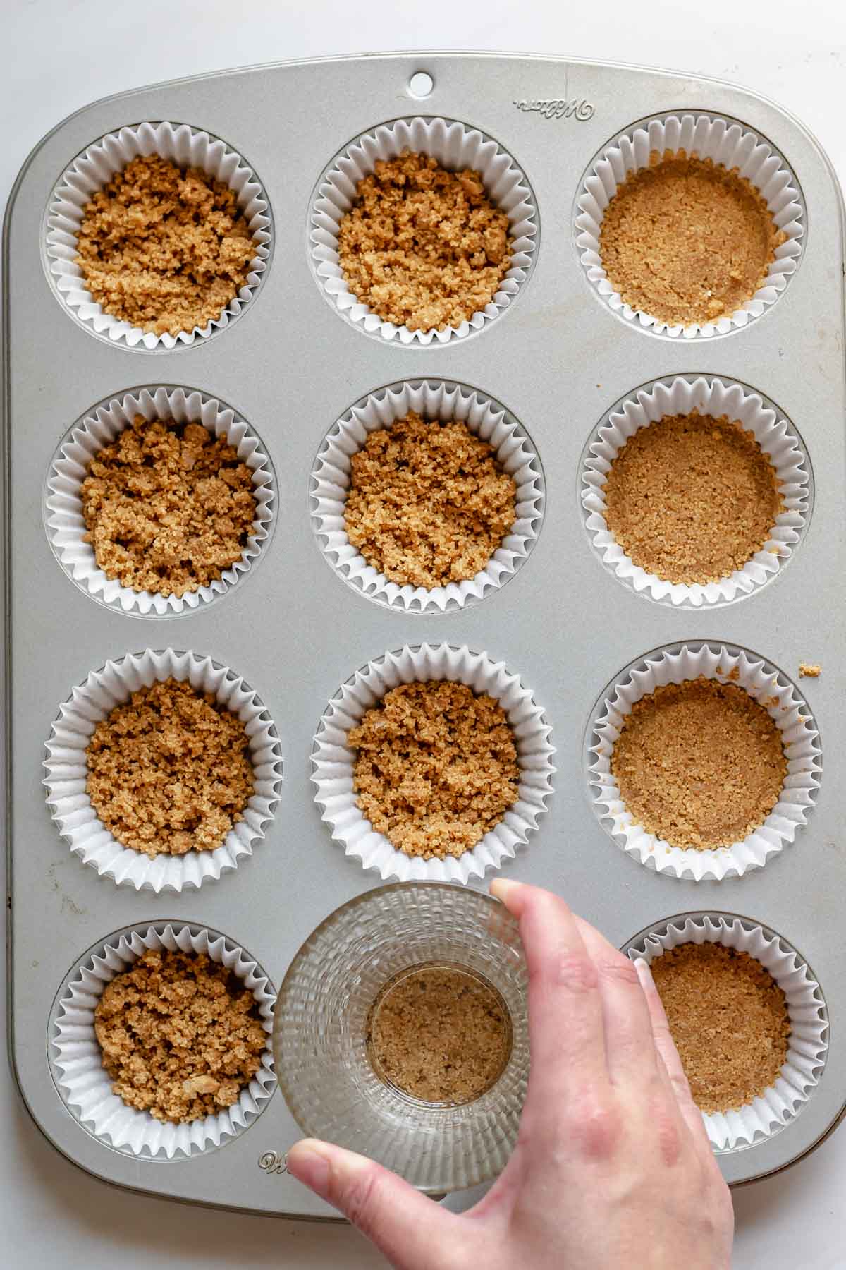 Graham cracker crumbs being pressed into a muffin tin.