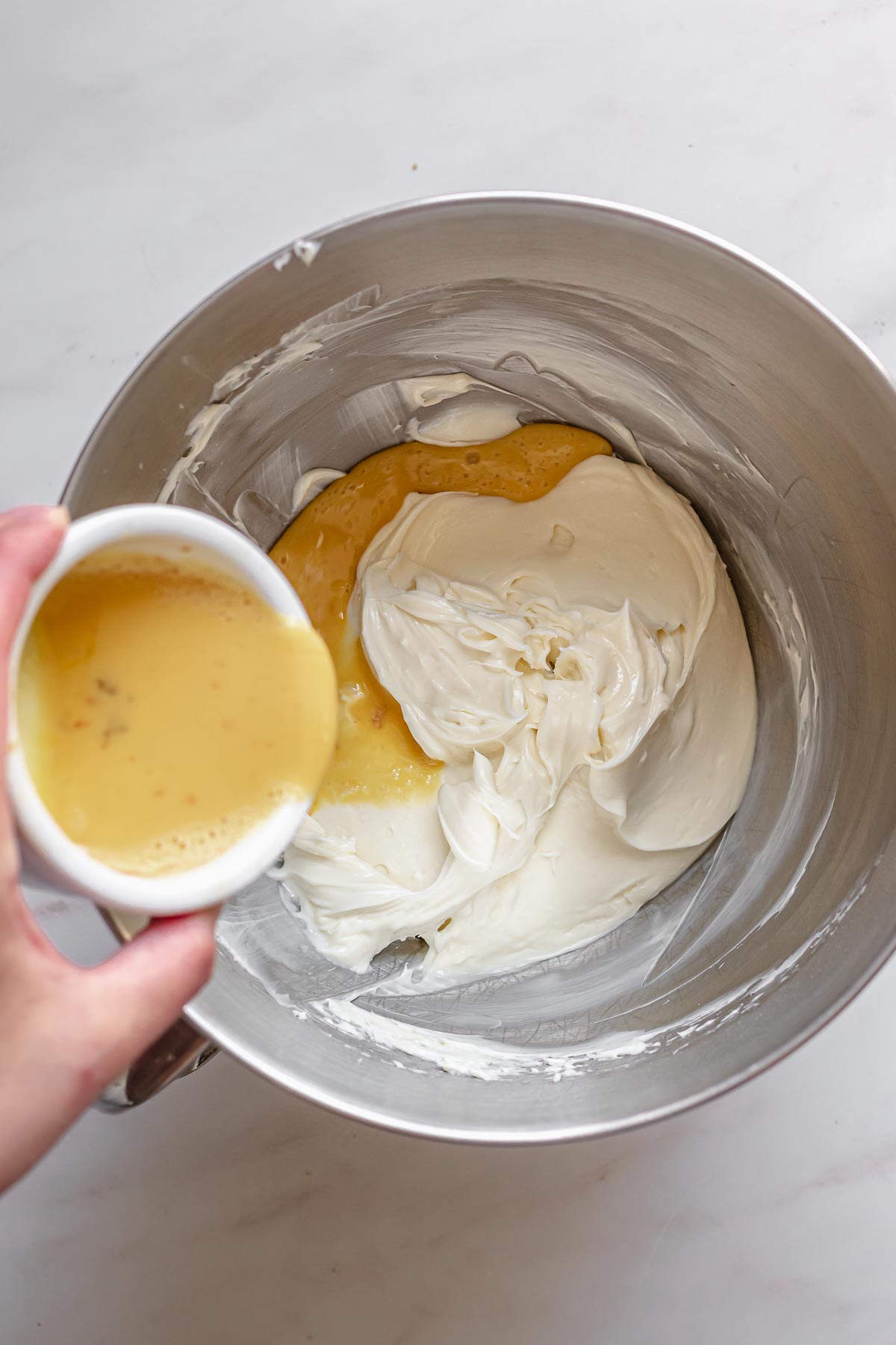 Whisked eggs being added to a bowl of cream cheese.