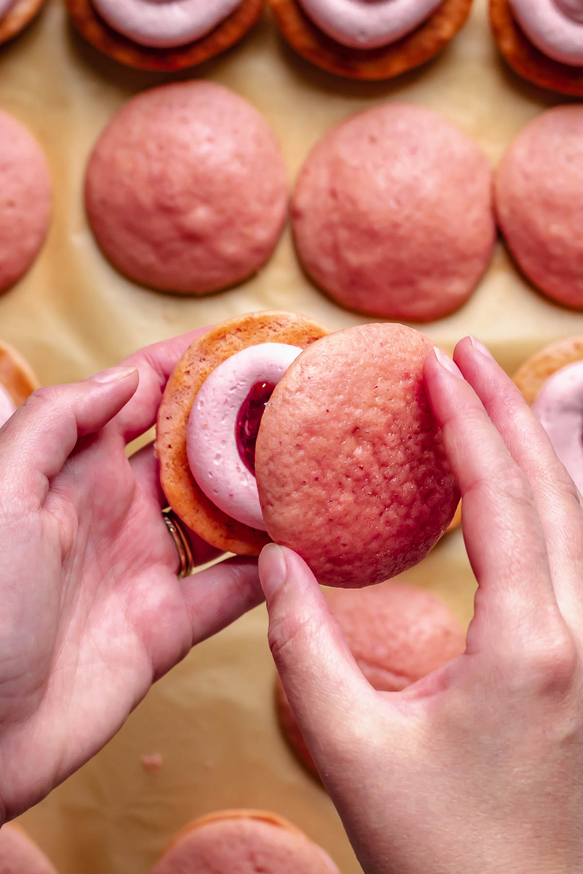 Hands close a strawberry whoopie pie.