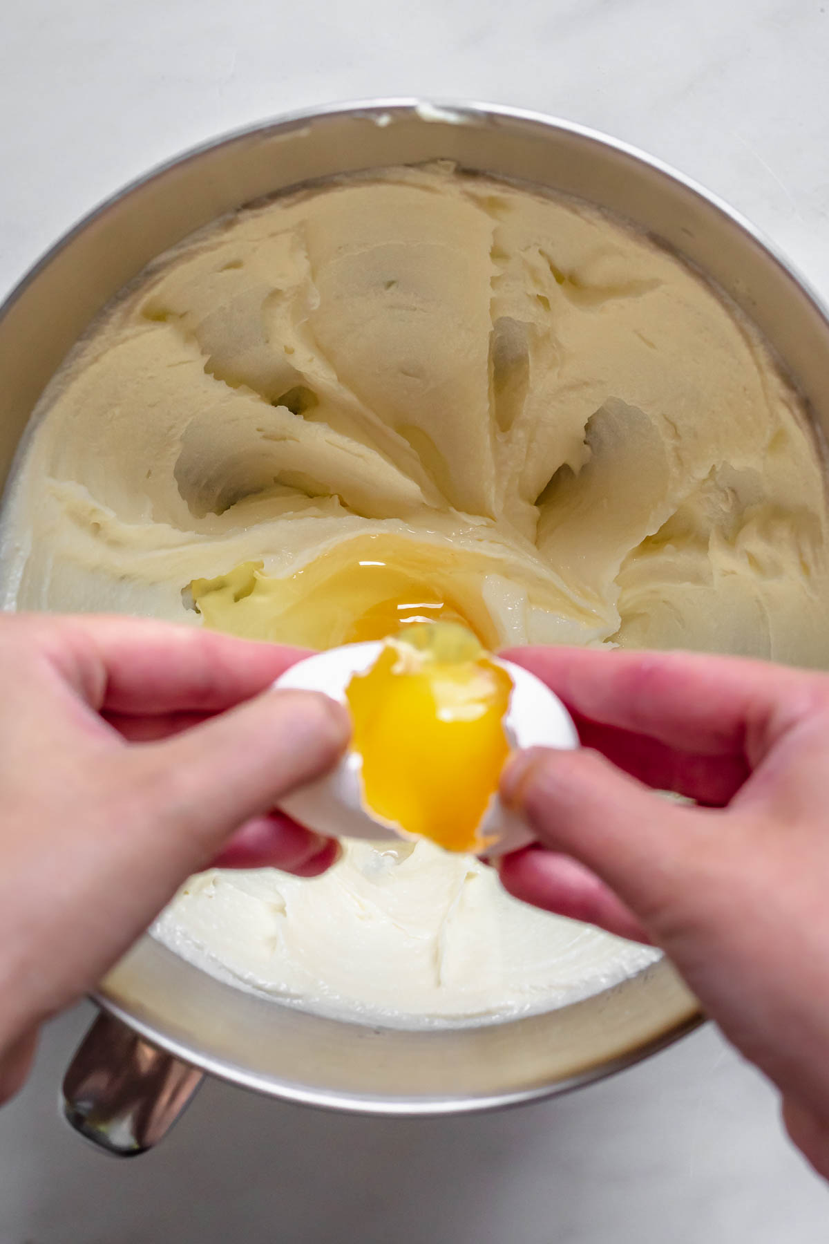 An egg cracking into a bowl of mixed butter.