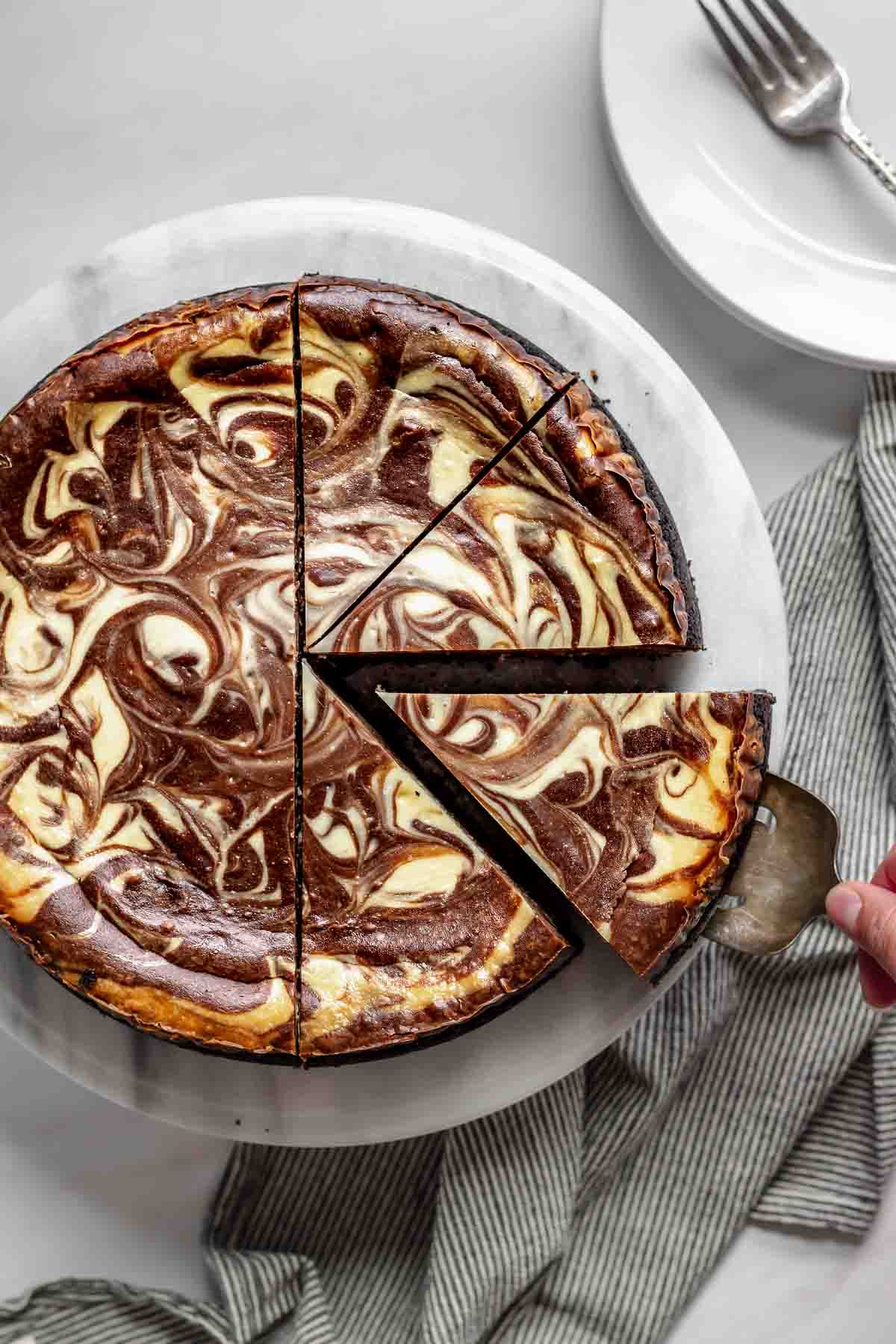 A slice of chocolate marble cheesecake being removed from a platter.