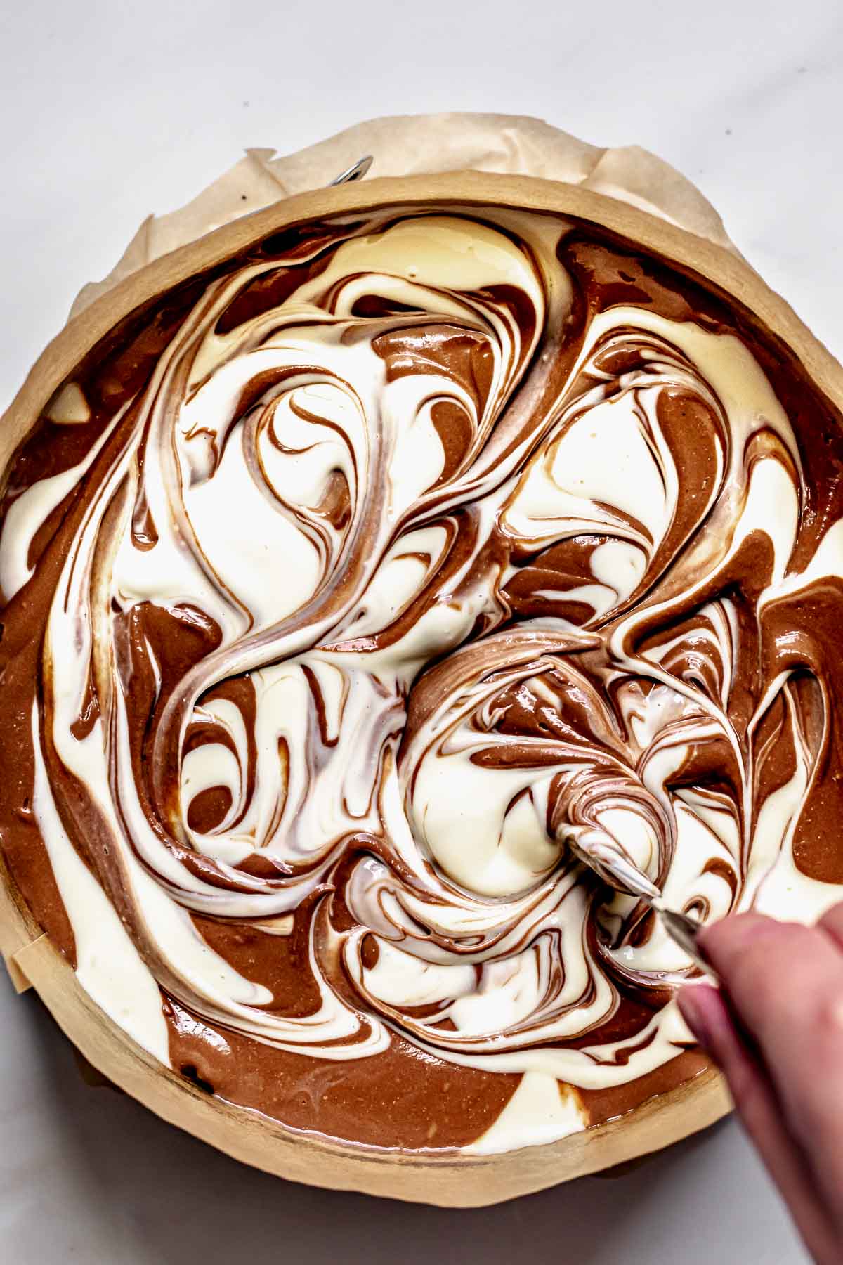 A knife creates a swirl pattern into the  cheesecake batter.