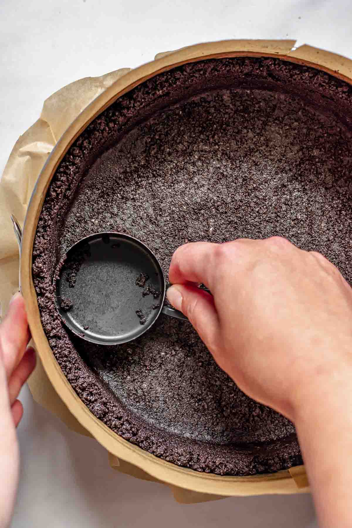 Pressing oreo crumbs into a springform pan.