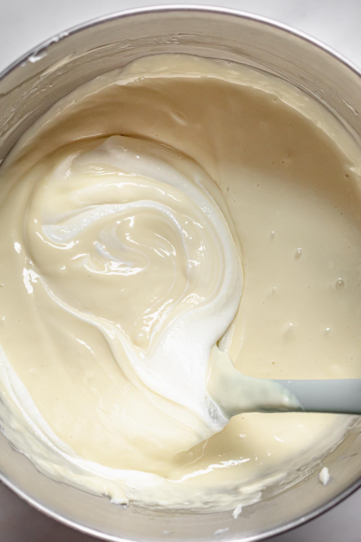 A spatula folds sour cream into cheesecake batter.
