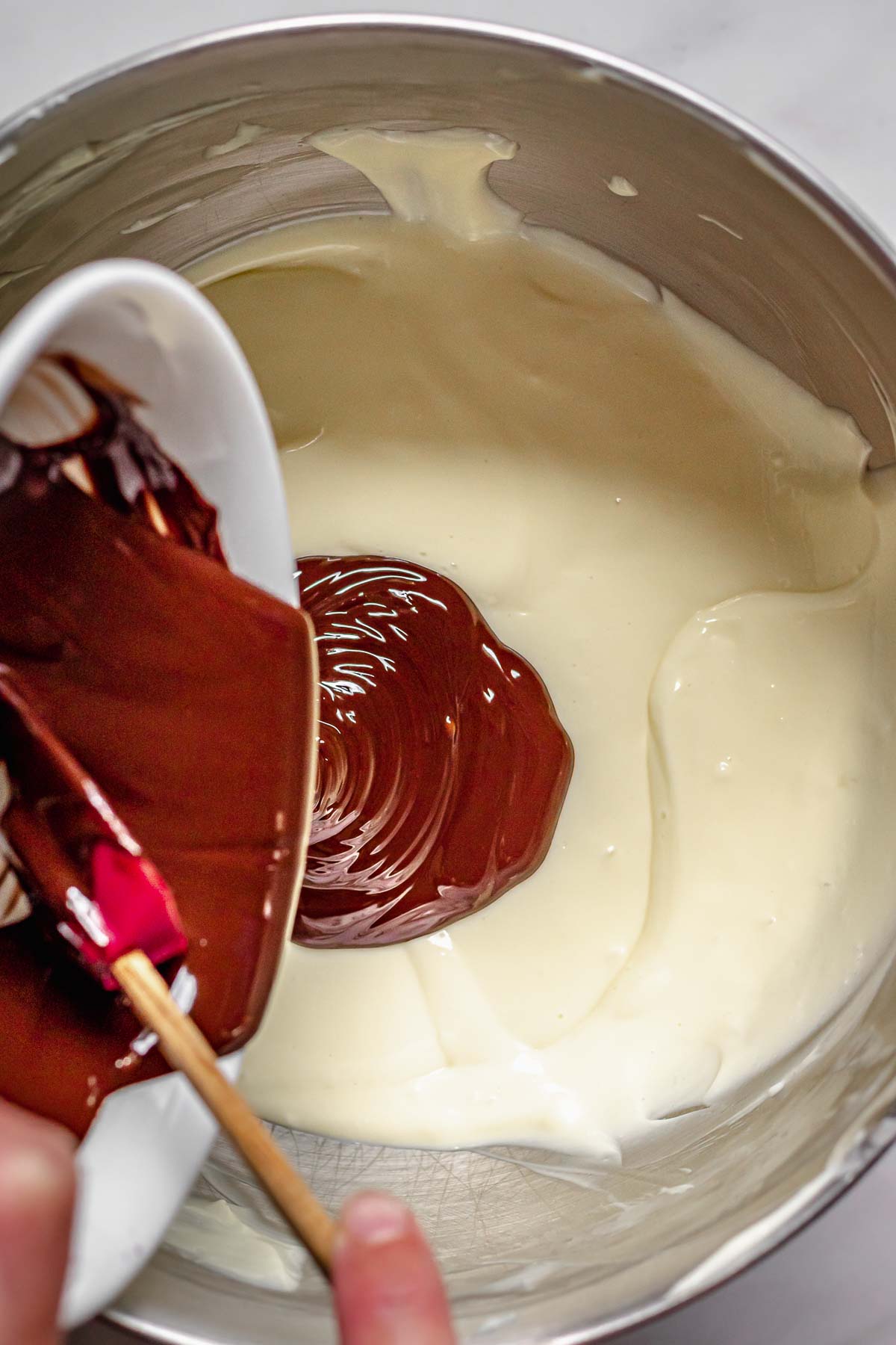 Melted chocolate being poured into cheesecake batter.
