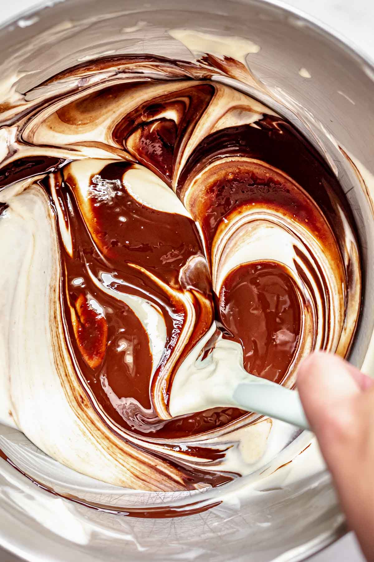 A spatula folds melted chocolate into chocolate cheesecake batter.