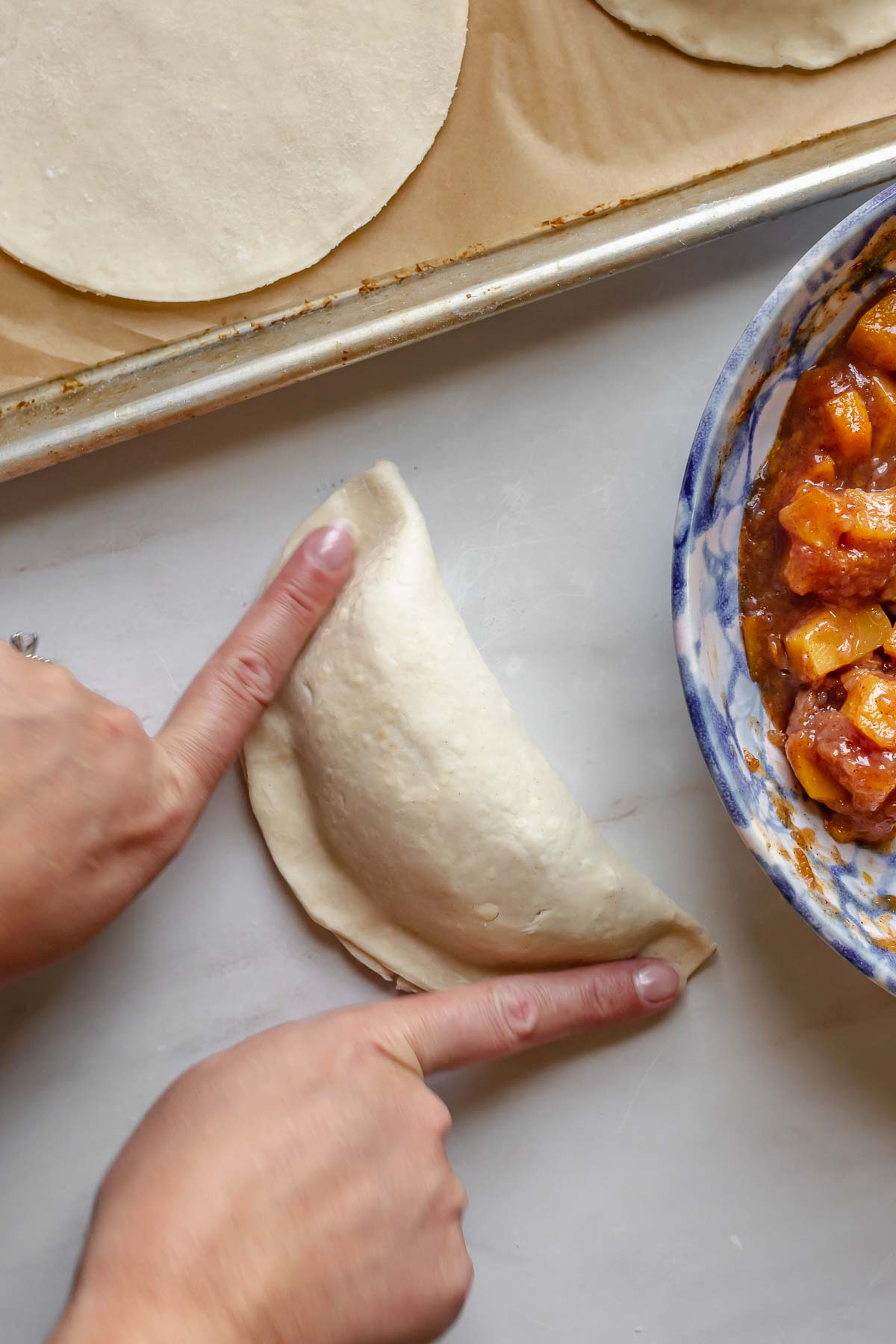 Fingers press down to seal the edges of the peach hand pie.