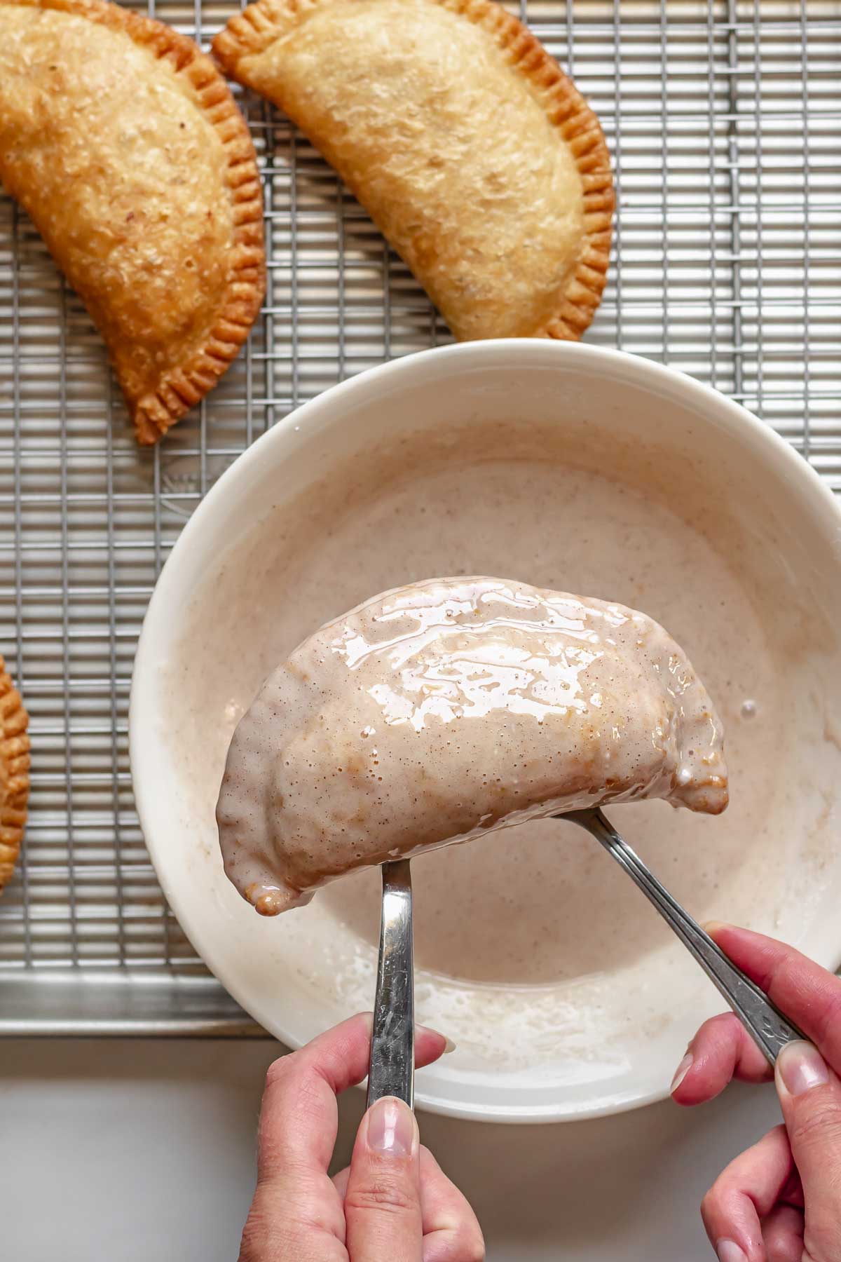 Two forks lifting a glazed fried peach pie out of a bowl.