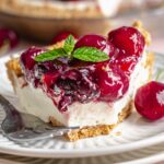 Slice of no bake cherry cheesecake pie on a plate with a bite removed.