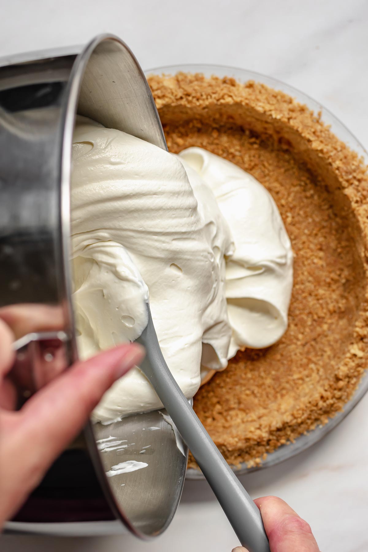 Cheesecake mixture being poured into a graham cracker crust.