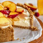 Sliced no bake mascarpone cheesecake on a platter with peaches on top.
