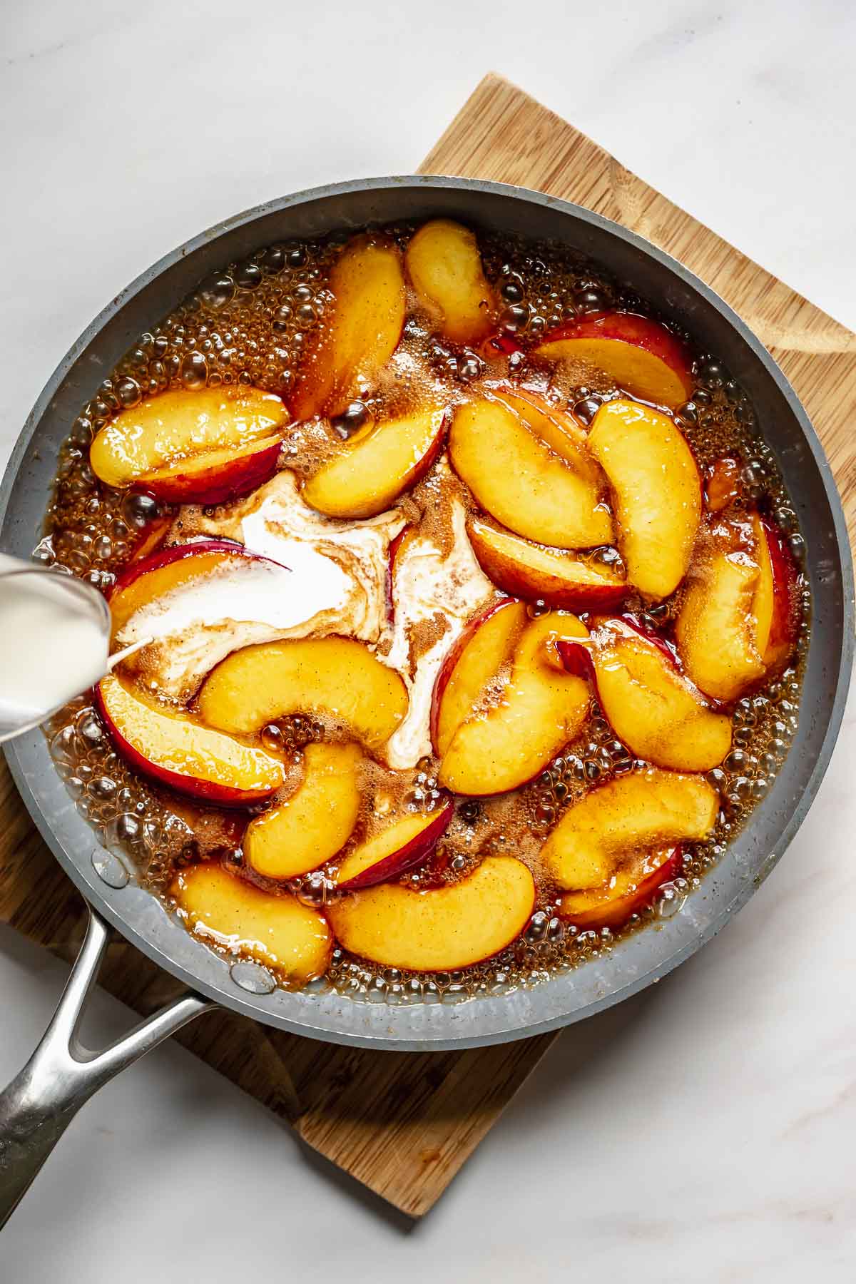 Heavy cream pouring into caramelized peaches.