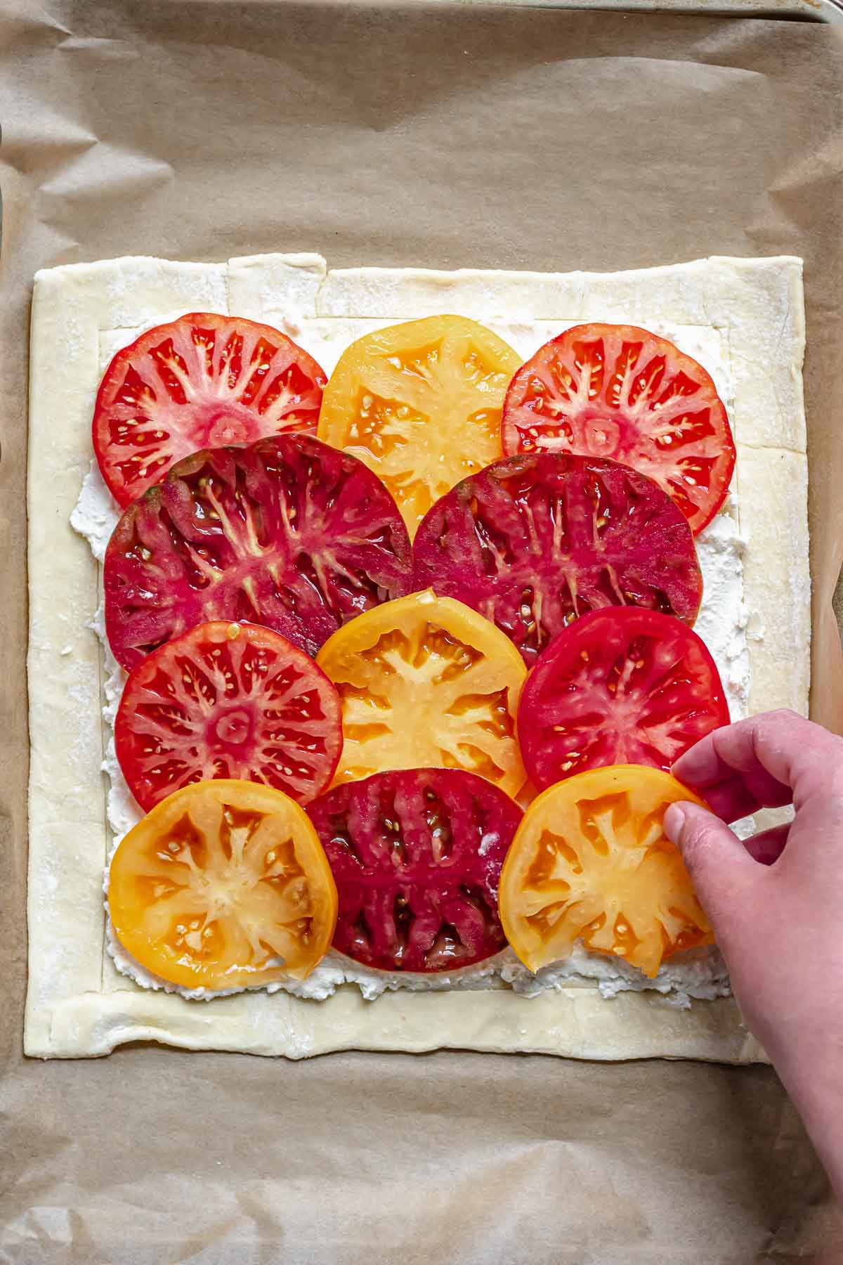 A hand adds sliced tomatoes on top of the cheese.